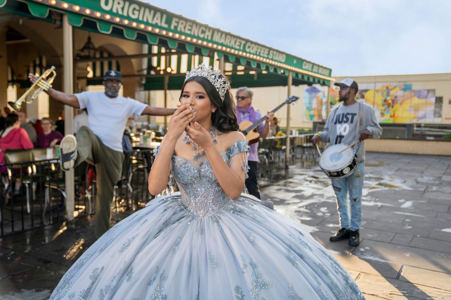 A young woman in a blue quinceañera gown and tiara enjoys a treat outside Original French Market Coffee Stand.