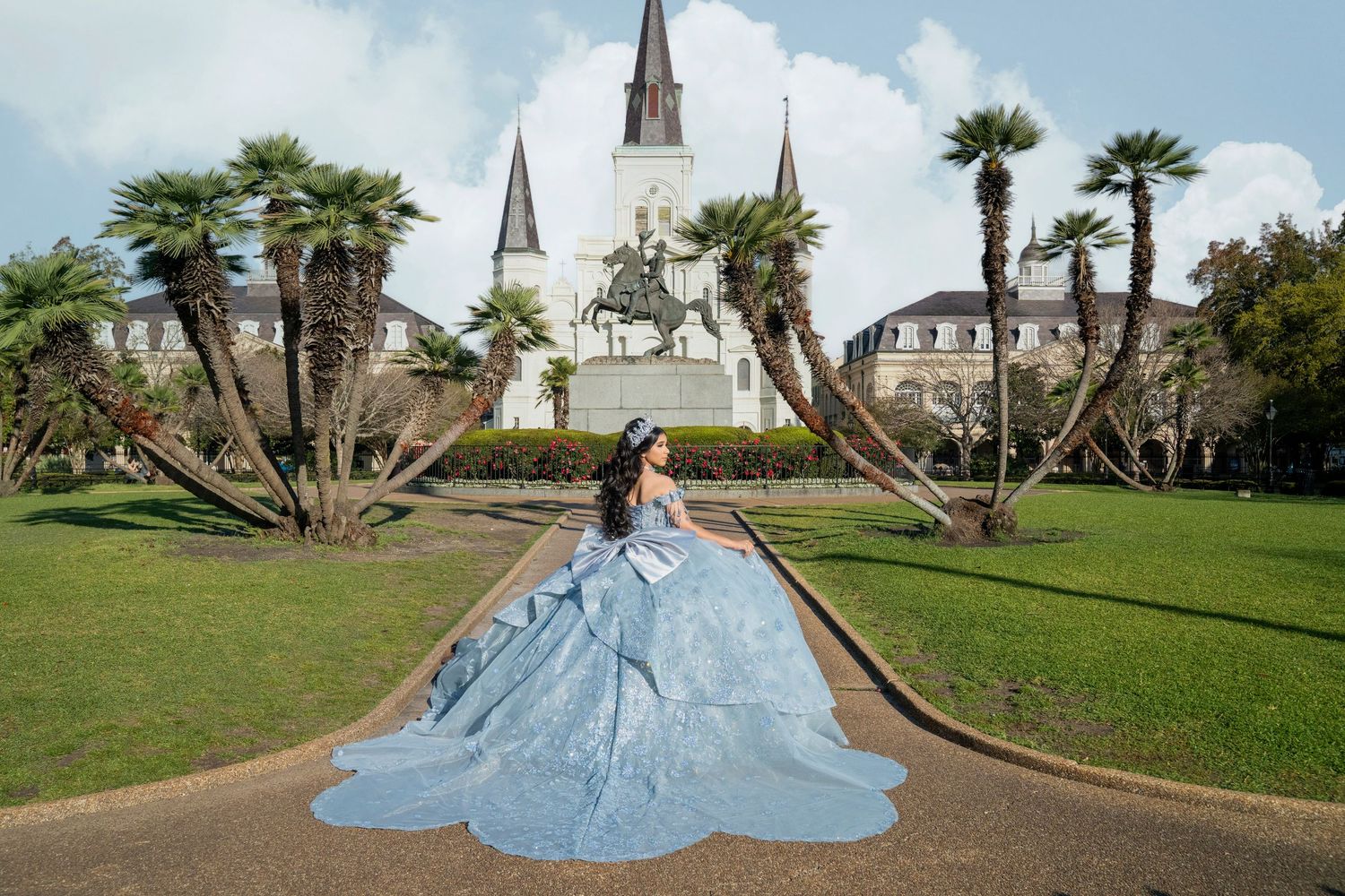 Young woman in a blue quinceañera ball gown poses in Jackson Square, New Orleans, with St. Louis Cathedral backdrop.