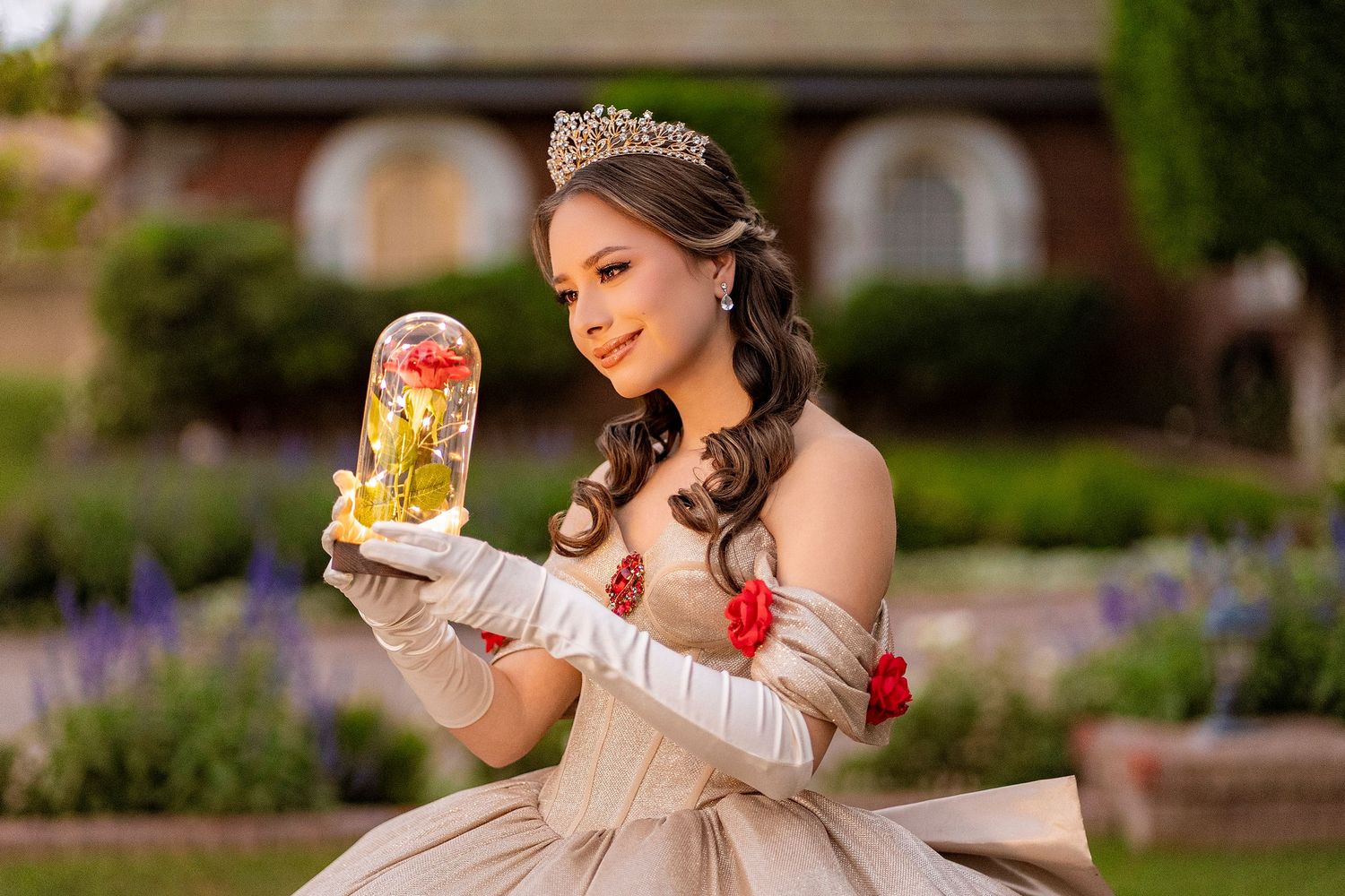 Woman in Belle costume holding enchanted rose dome in garden setting.
