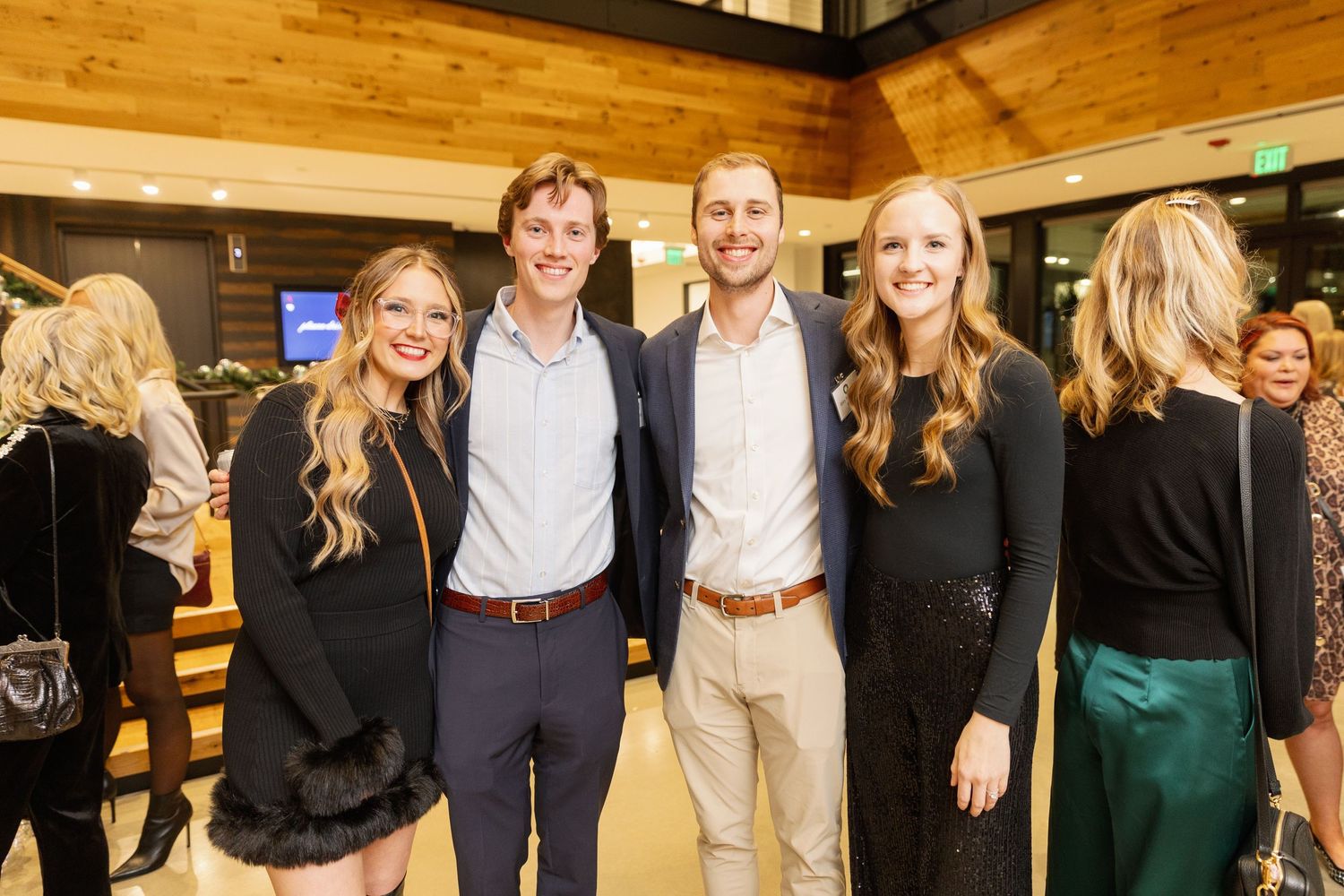 Group of people smiling at indoor event wearing business casual attire standing together in wood-paneled venue.