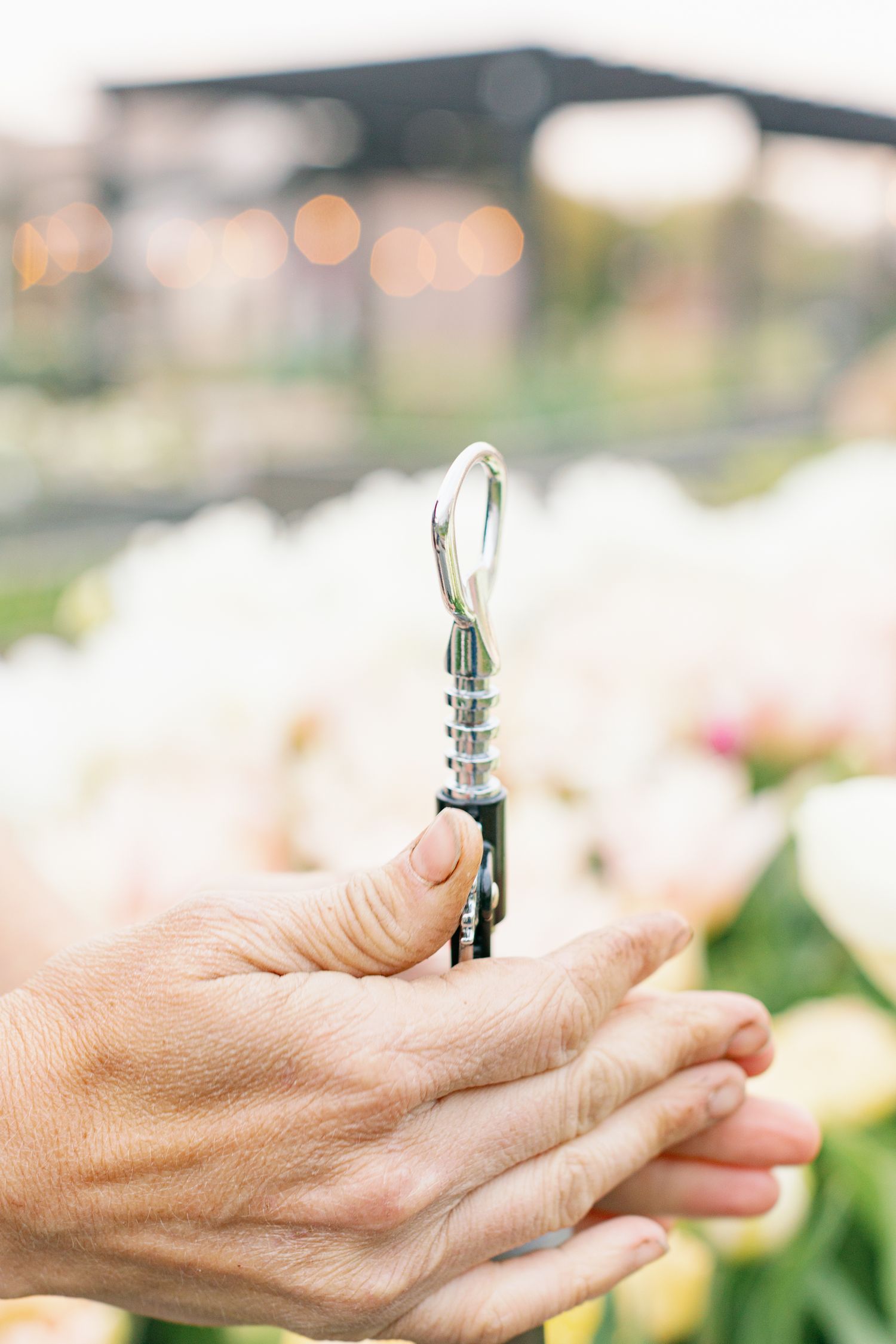Hands hold a silver vintage wine bottle opener against a soft blurred background with bokeh lights.