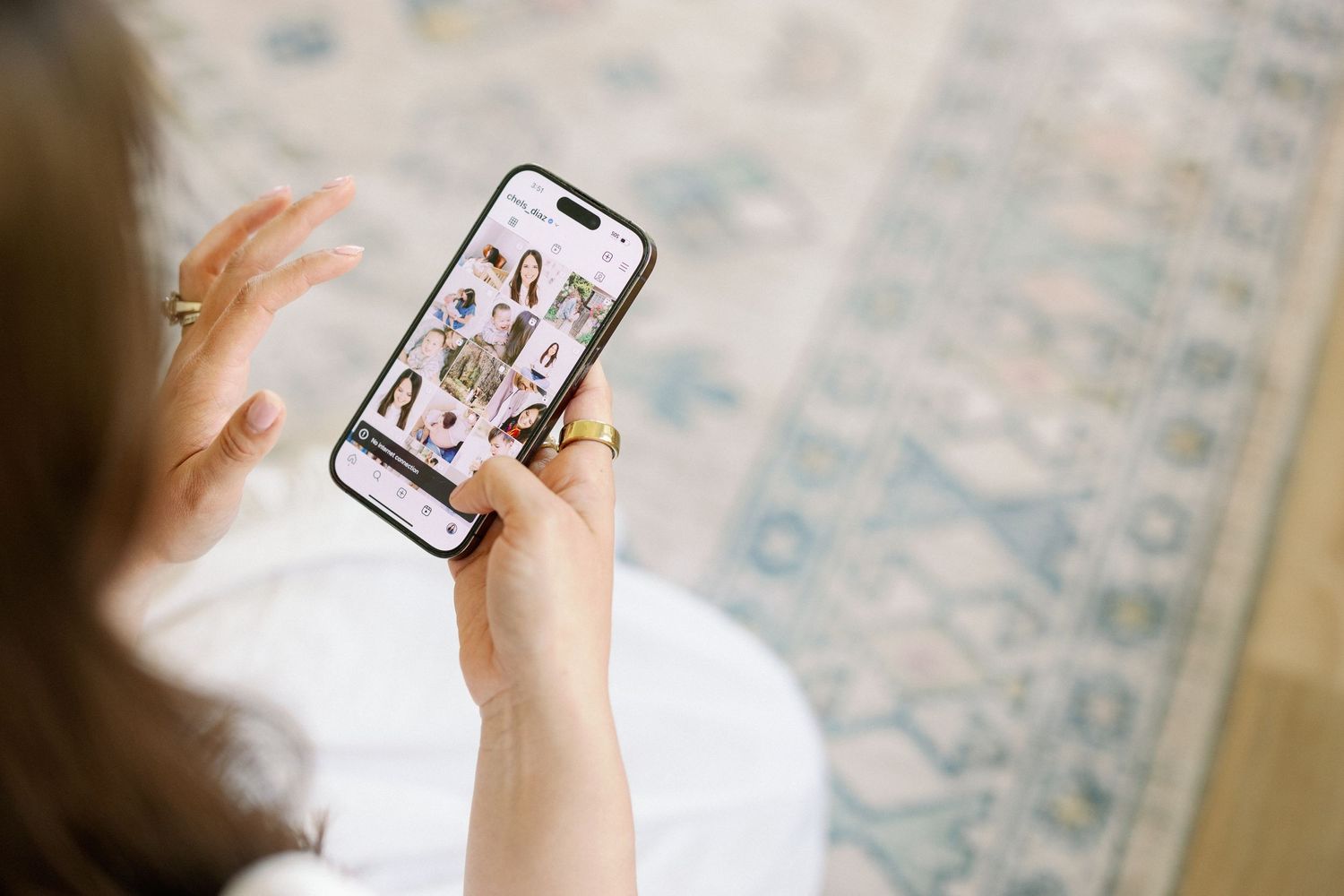 Person holding smartphone displaying social media or video chat app interface while sitting on patterned carpet.