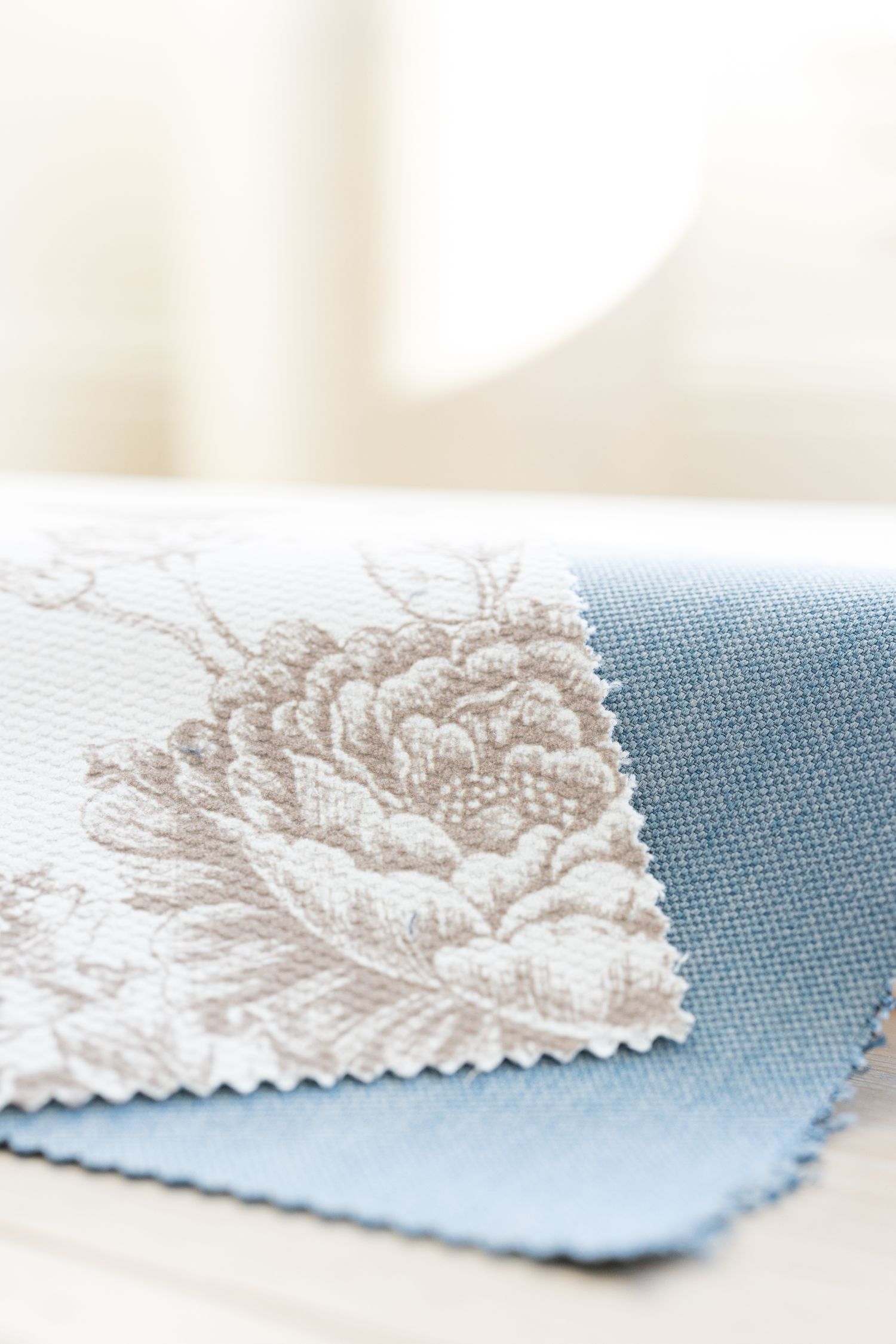 Close-up of floral patterned fabric swatch in beige next to light blue fabric material.