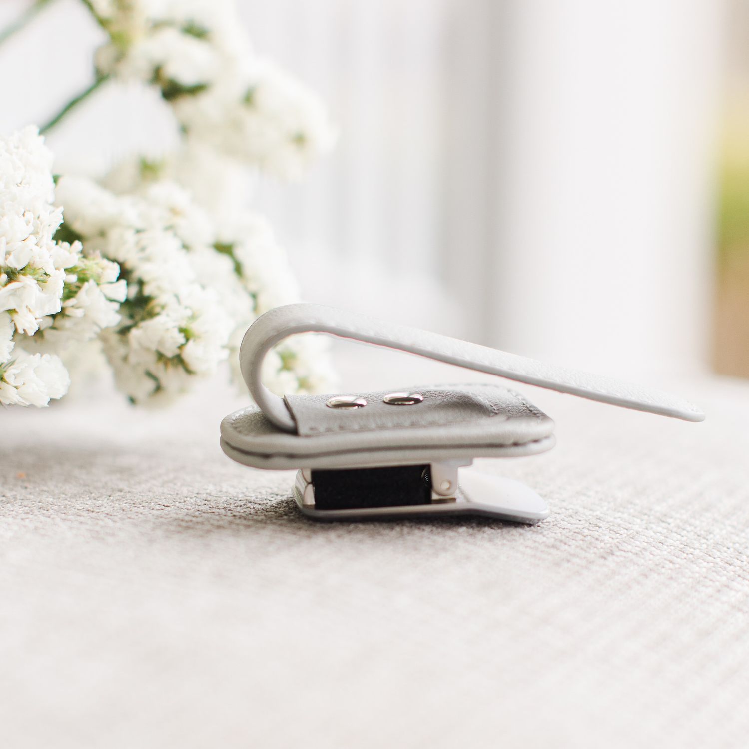 Silver paperclip holding papers with delicate white flowers in soft focus on textured fabric background.