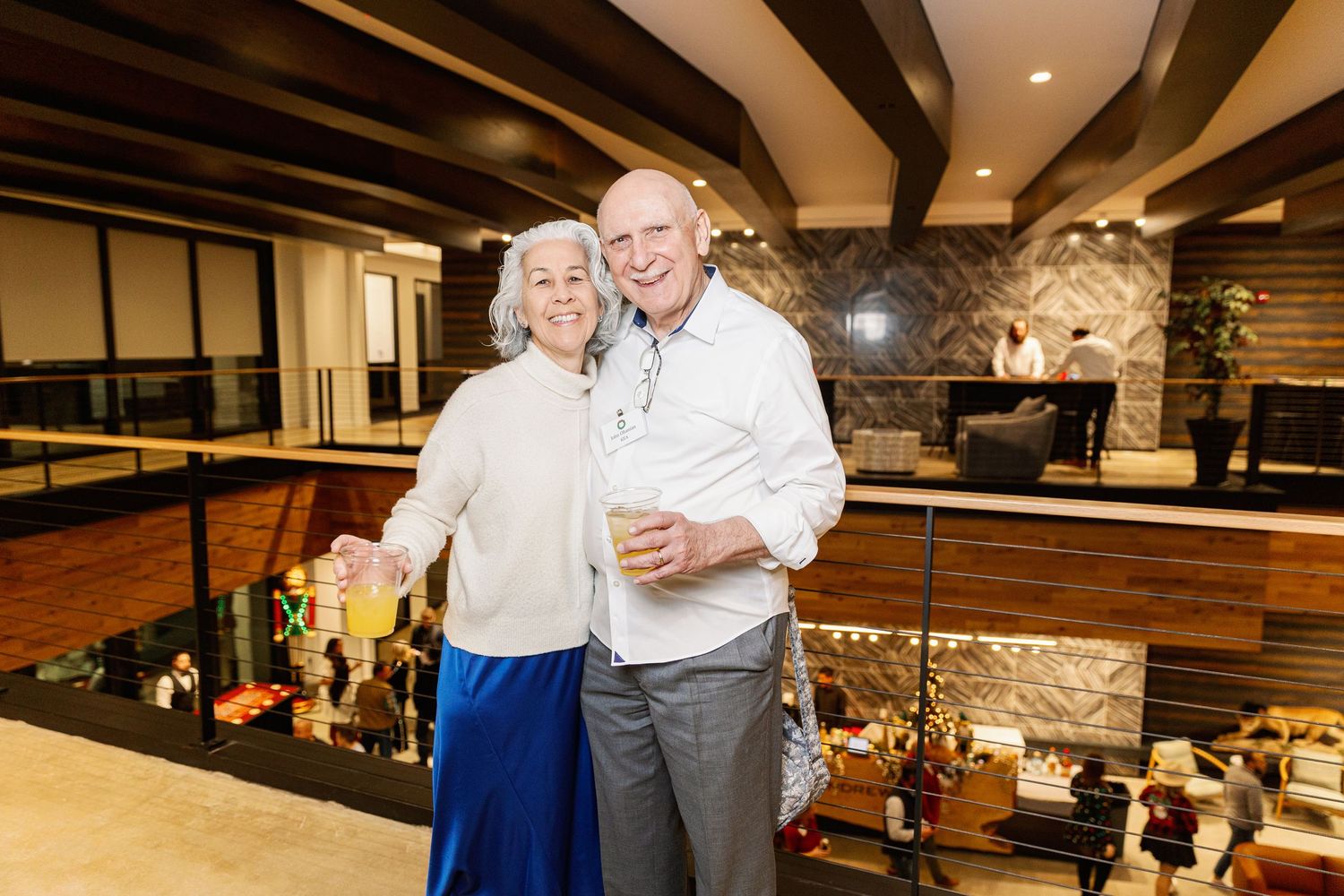 Two people pose together in a modern restaurant interior with exposed wood beams and stone accent walls.