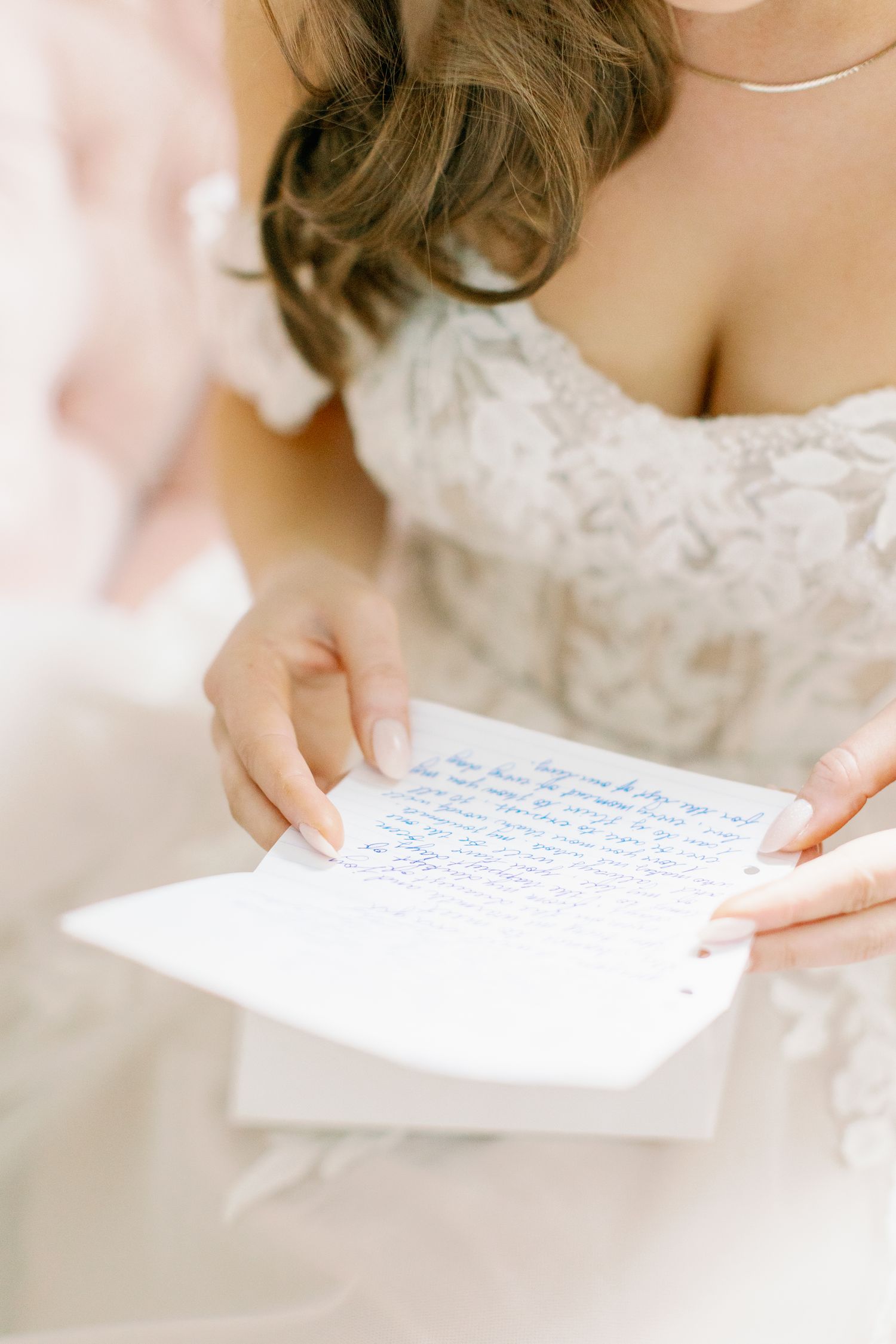 A bride in a white lace dress reads a handwritten letter on her wedding day.