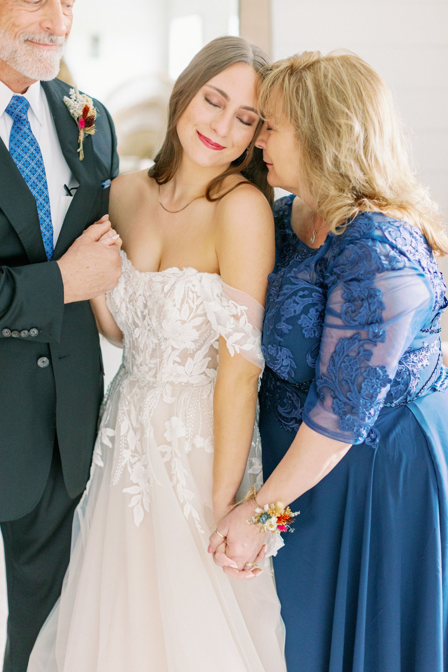 A tender family moment on a wedding day with a couple embracing their daughter in an elegant off-shoulder lace gown.