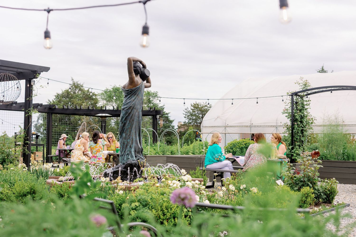 Outdoor garden gathering with string lights overhead as people enjoy a social event among lush greenery at a restaurant patio.