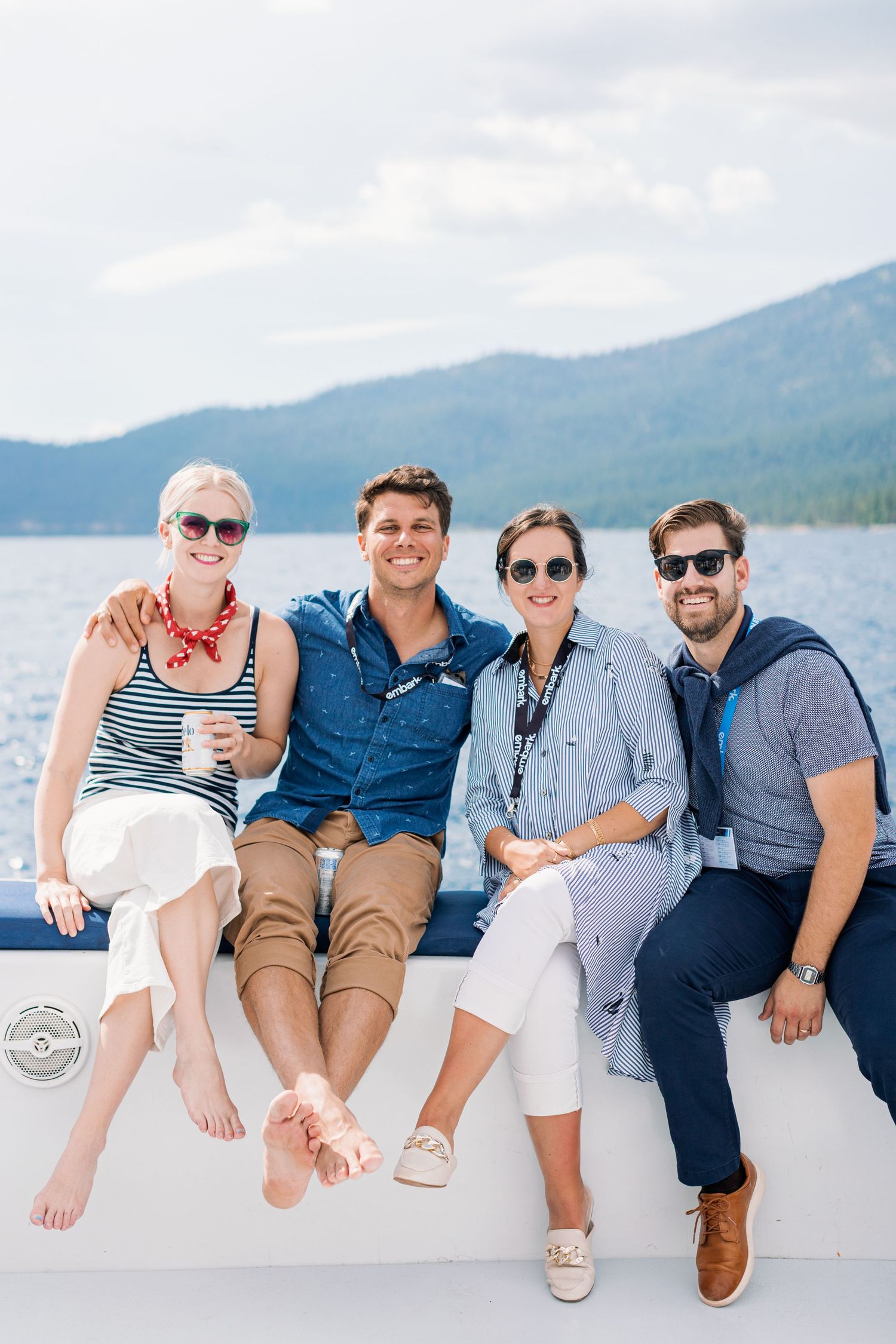 People enjoying a sunny day sitting together on a boat with mountains and a lake in the background.