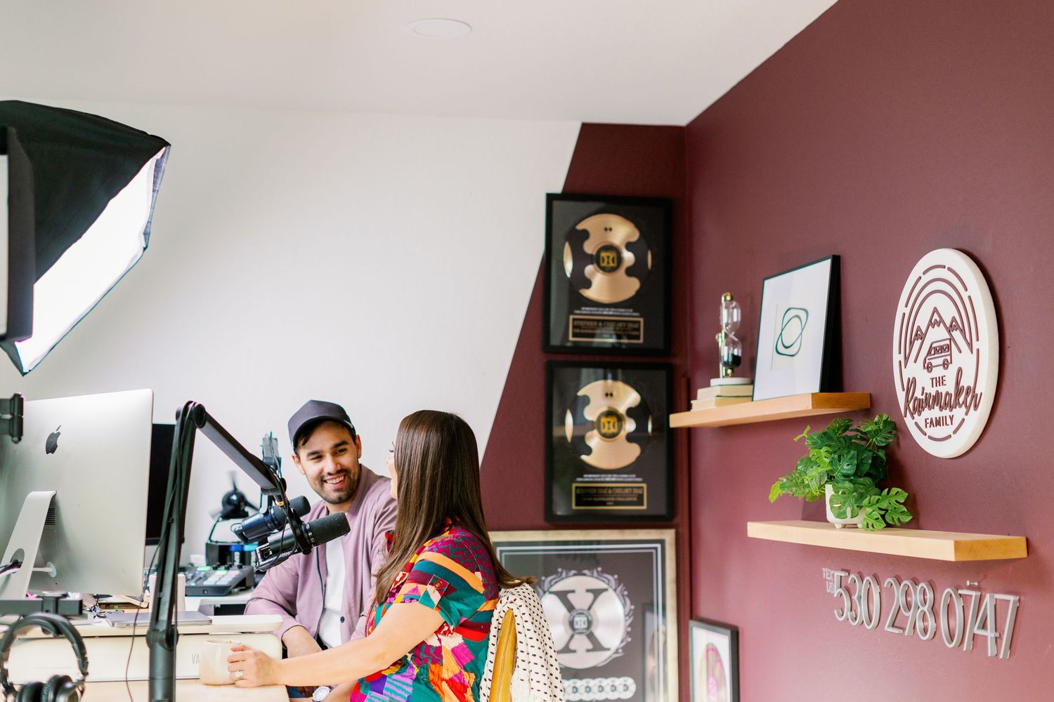 Two people working at a creative office space with pink walls decorated with framed artwork and wooden shelves.