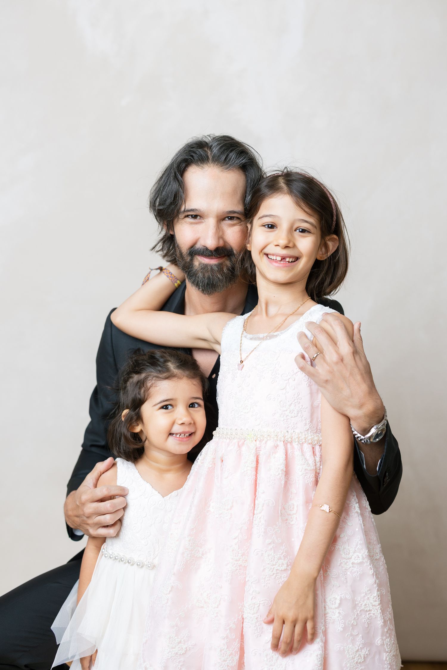 A family portrait against a light background showing affectionate embrace and warm smiles while wearing formal attire.
