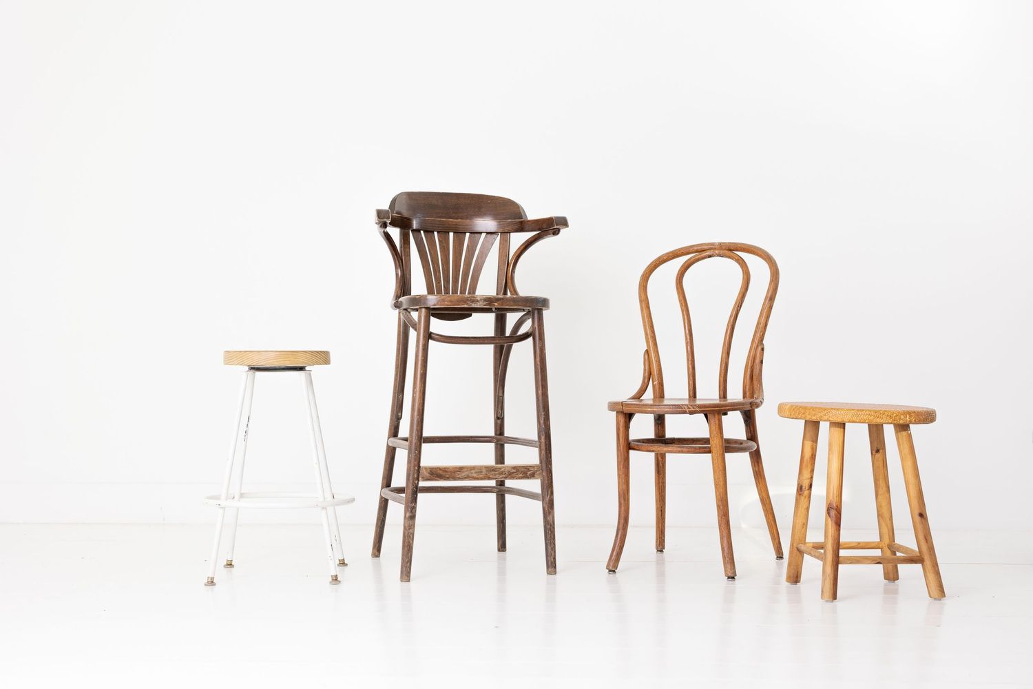 Four vintage wood chairs and stools in different styles and heights arranged on white background.