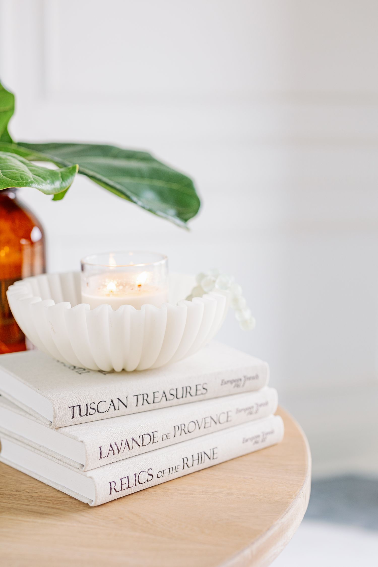 Stack of elegant coffee table books with 'Tuscan Treasures' and 'Lavande de Provence' topped with a white candle holder.