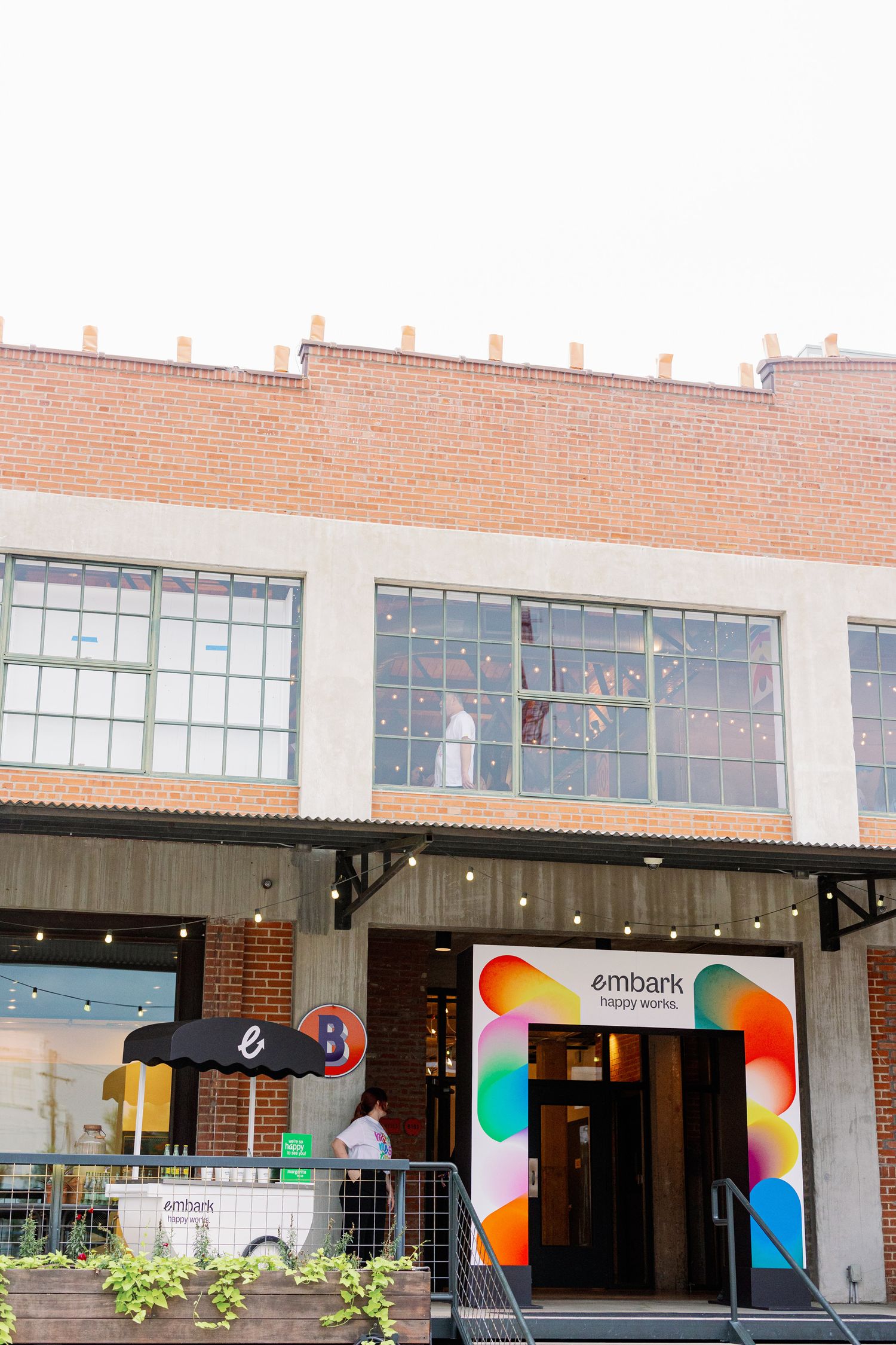 Modern brick building with colorful rainbow-patterned Embank storefront entrance and large industrial windows above.