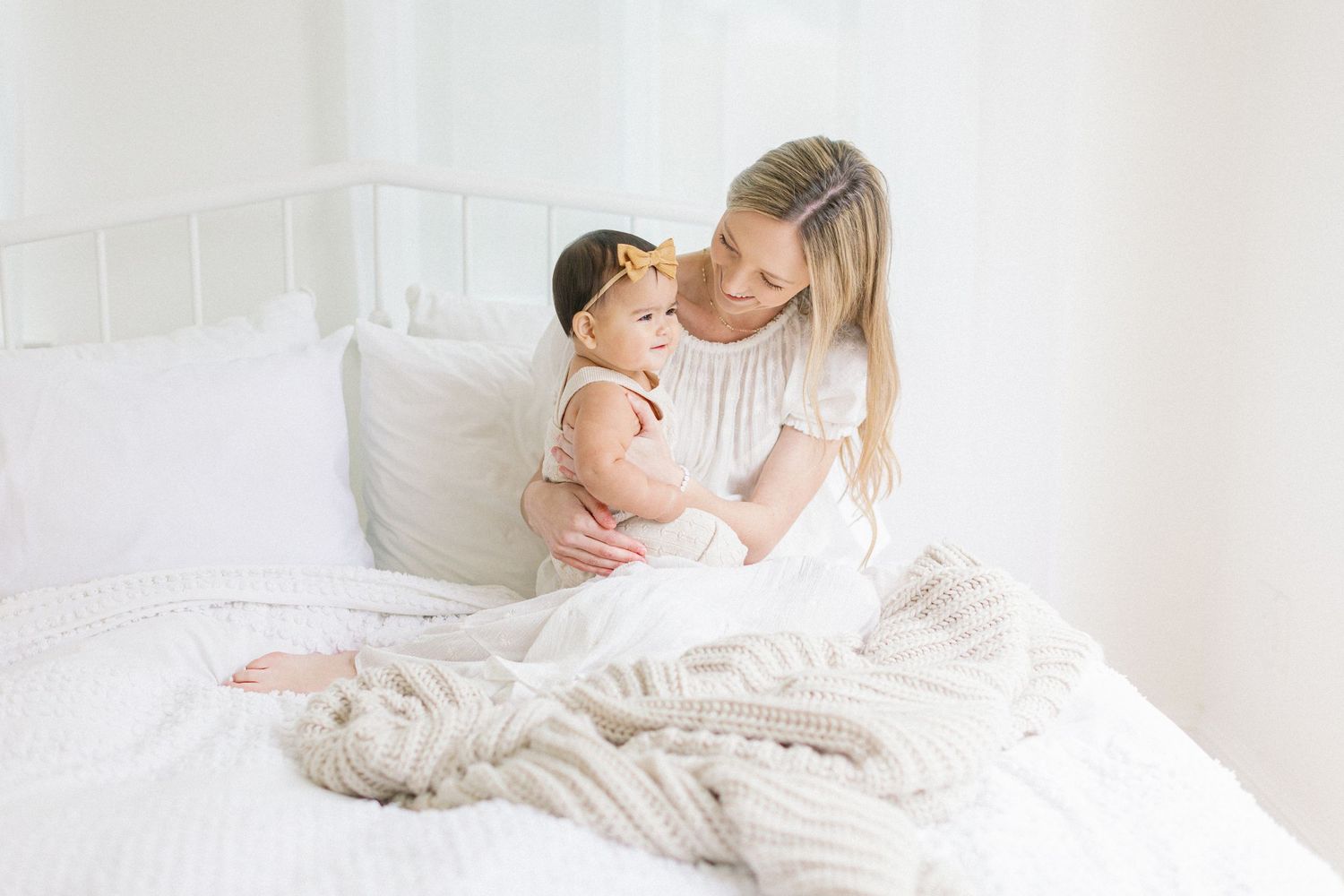 A tender moment between mother and baby on a white bed with a chunky knit blanket.