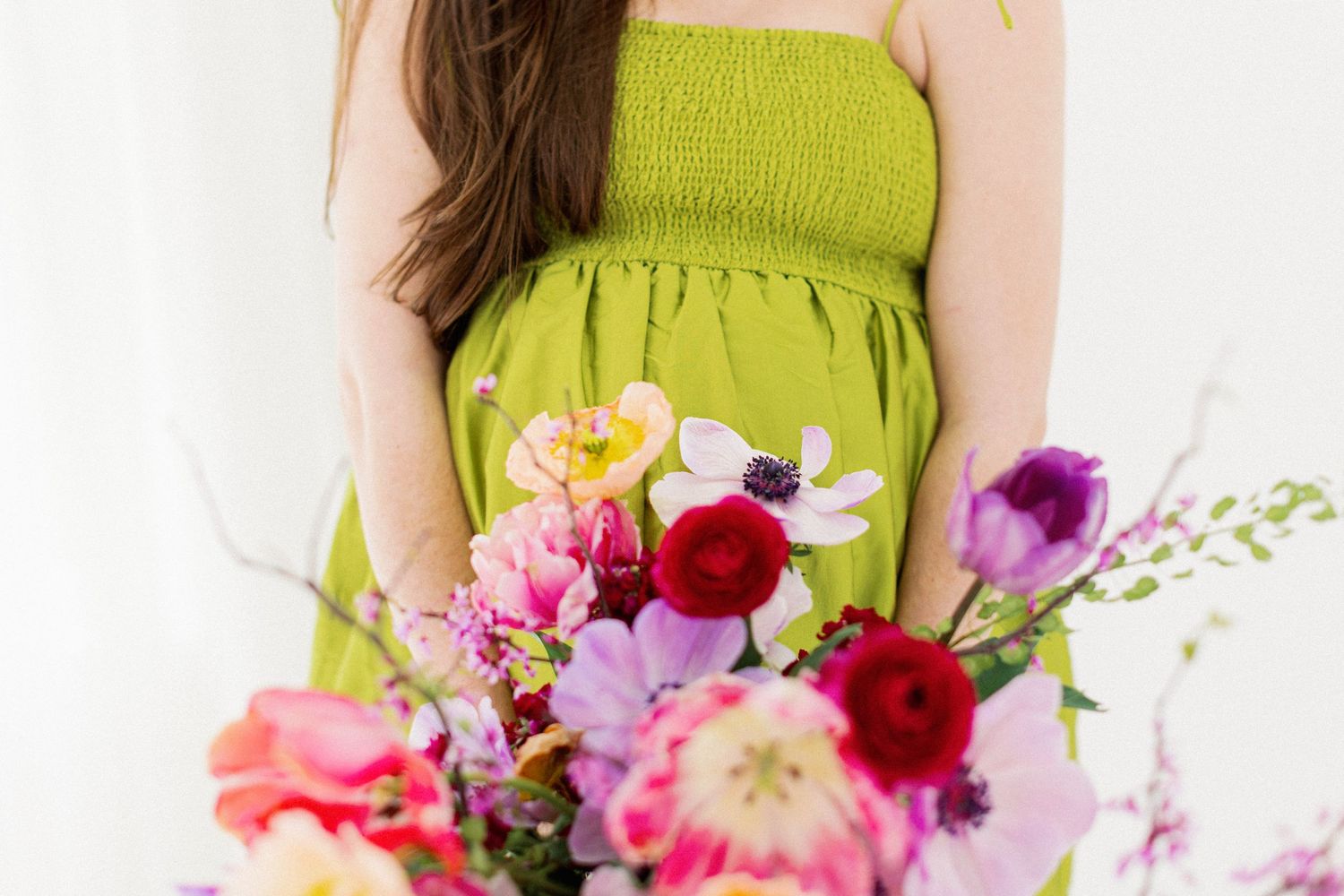 Vibrant spring bouquet with ranunculus, tulips and wildflowers held against a lime green dress on white background.