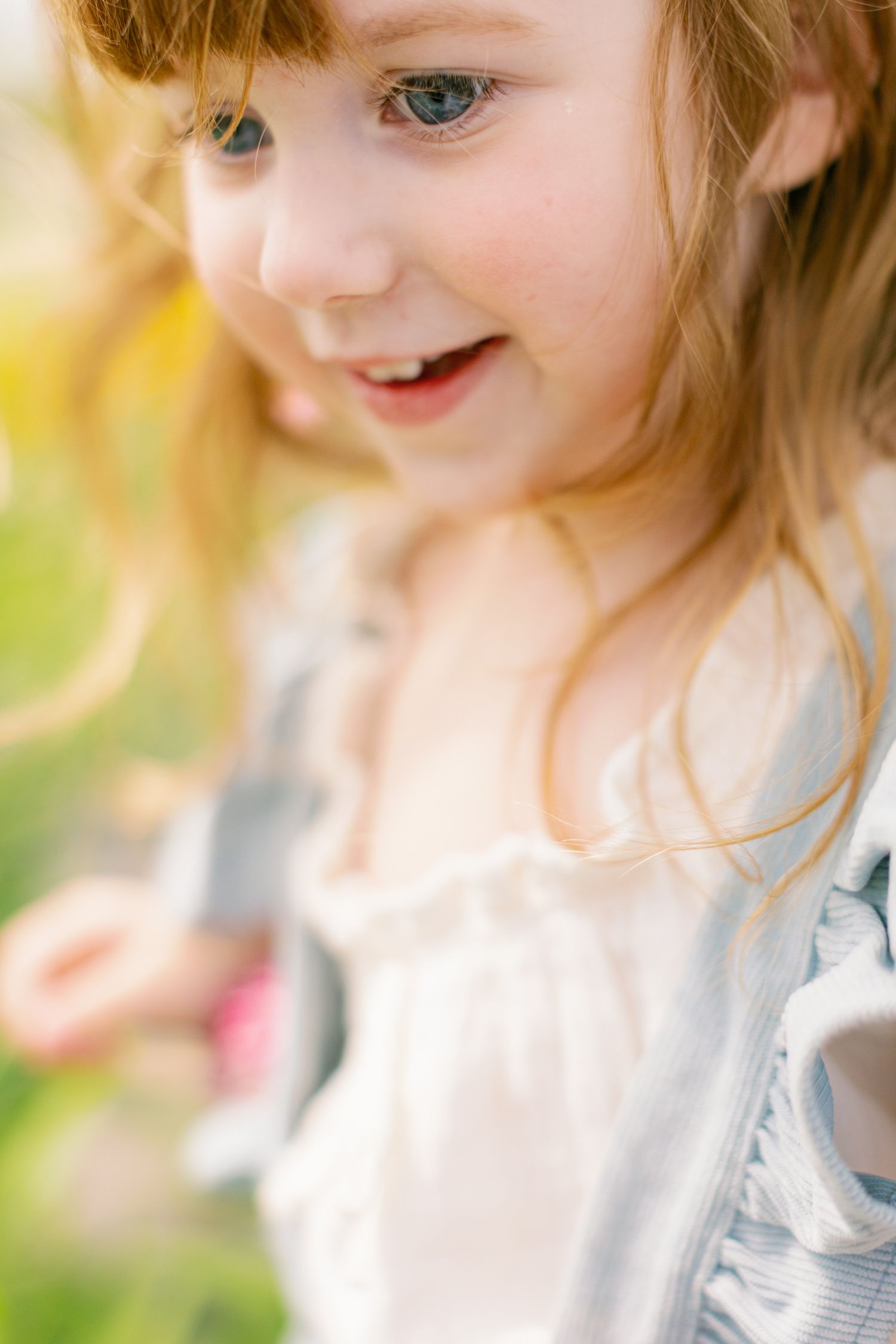 A close up portrait with bright blue eyes and soft smile against a dreamy yellow and green background.