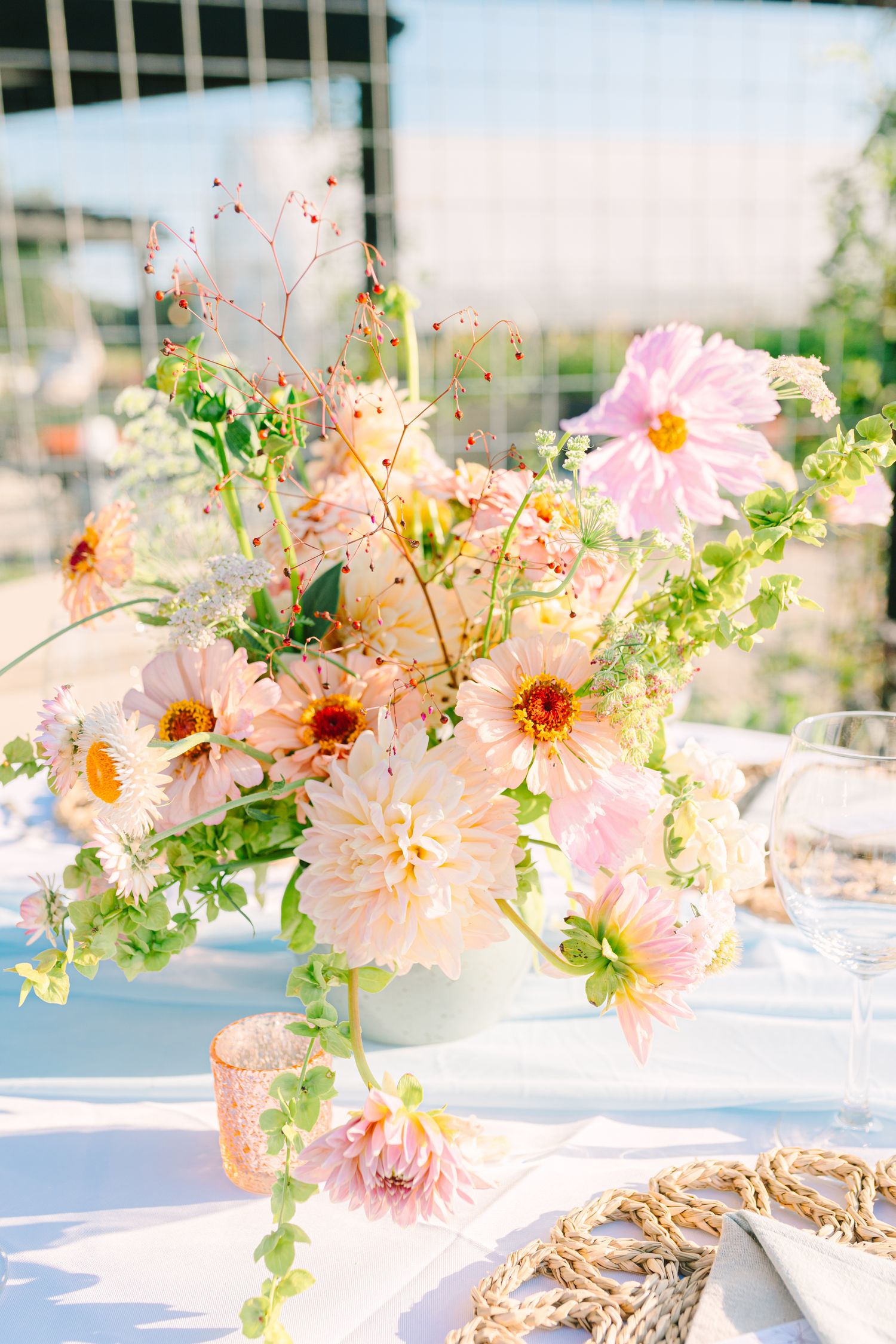 Soft pink dahlias and delicate wildflowers arranged in a white vase on a sunlit table with a vintage romantic aesthetic.