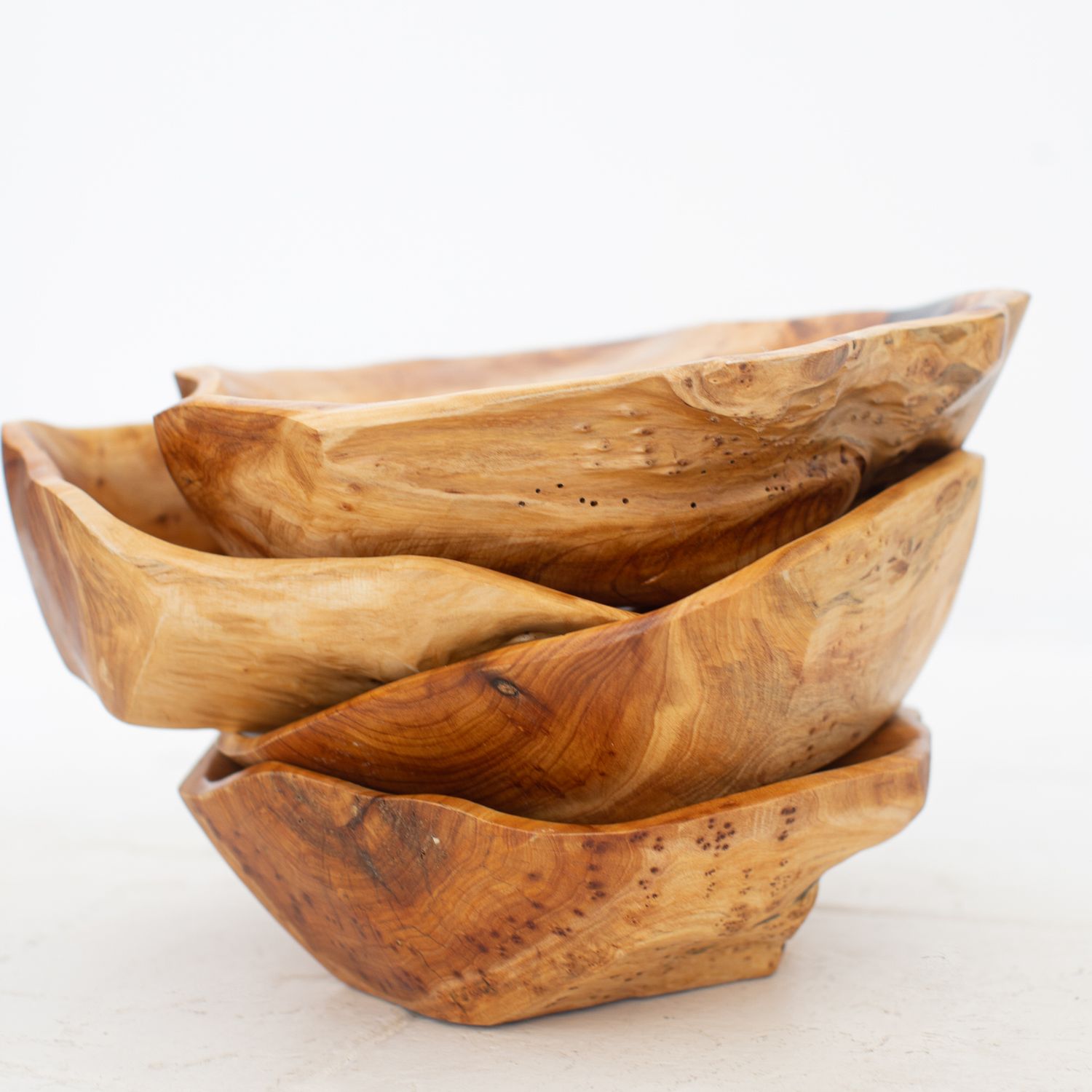Three rustic hand-carved wooden bowls made from natural wood stacked on each other in an artistic arrangement.