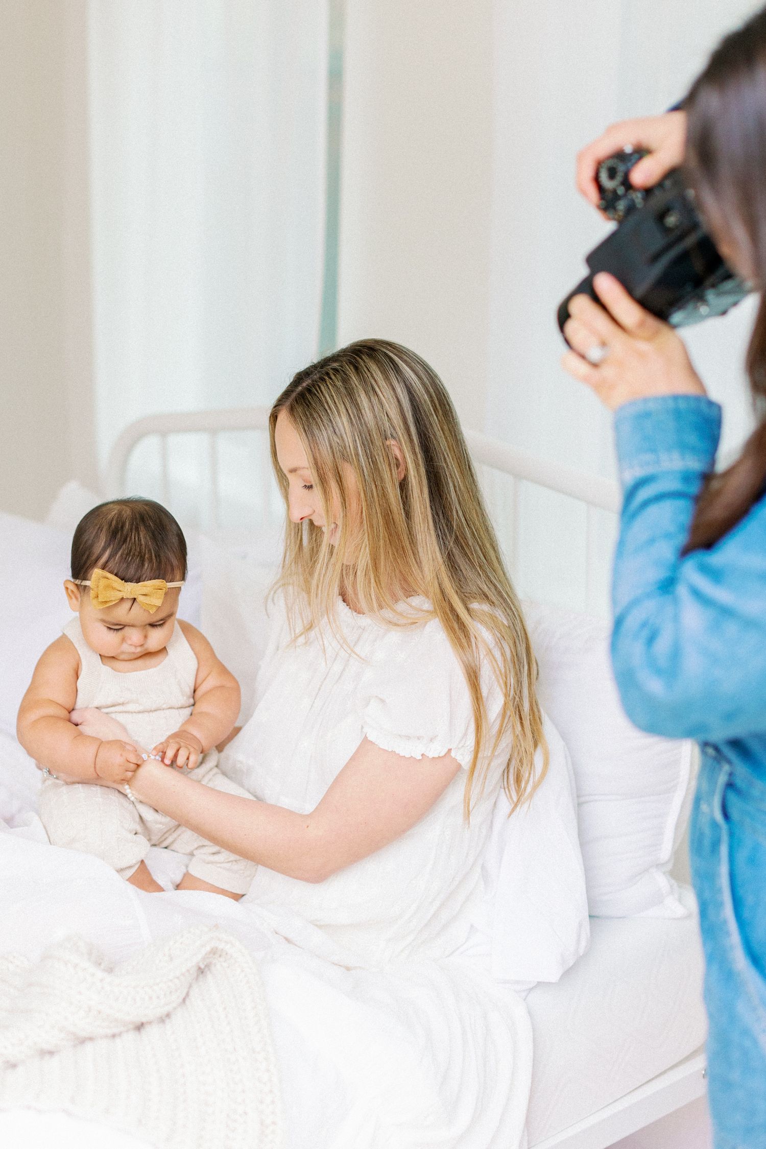 Photographer capturing candid moment of mother and baby sitting on white couch during indoor photo session.