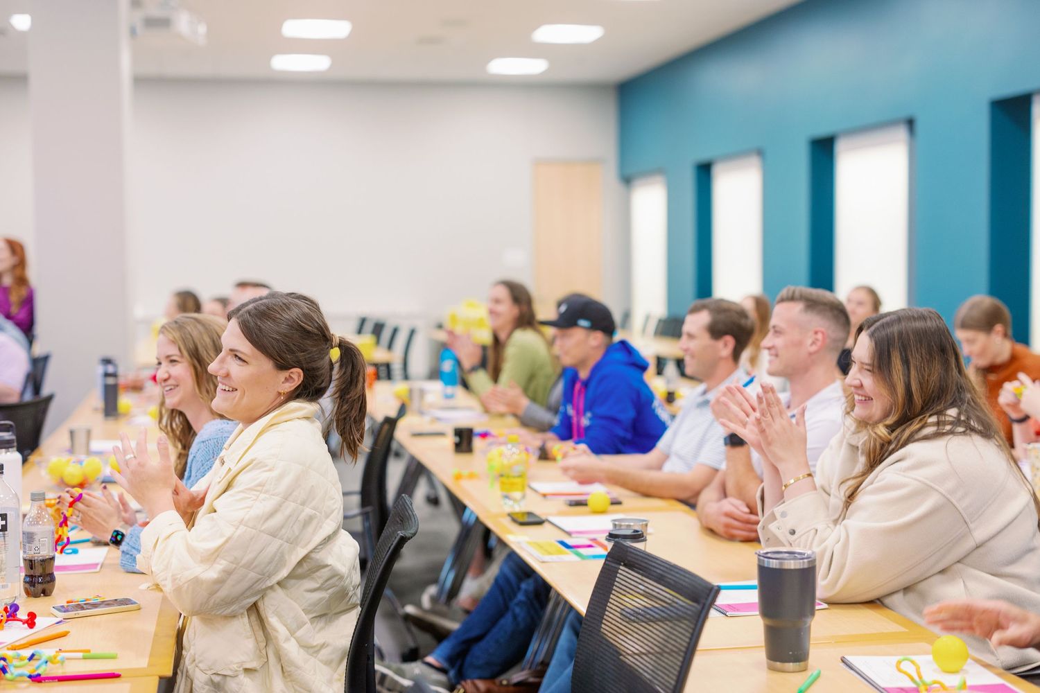 People sit at long tables in a meeting room with blue accent walls during a business or training session.