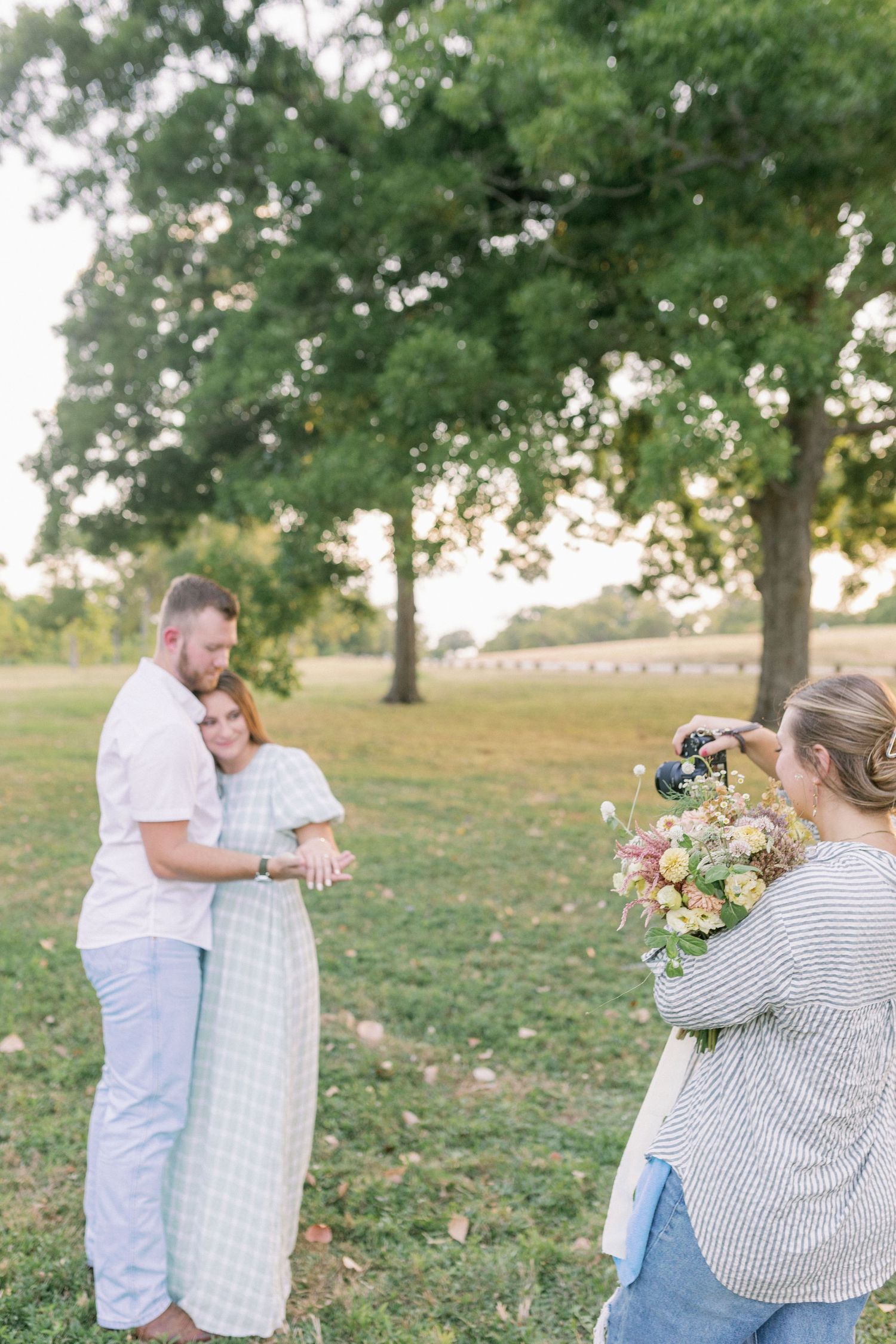Behind the scenes photo of a photographer capturing a couple in a natural outdoor setting with trees.