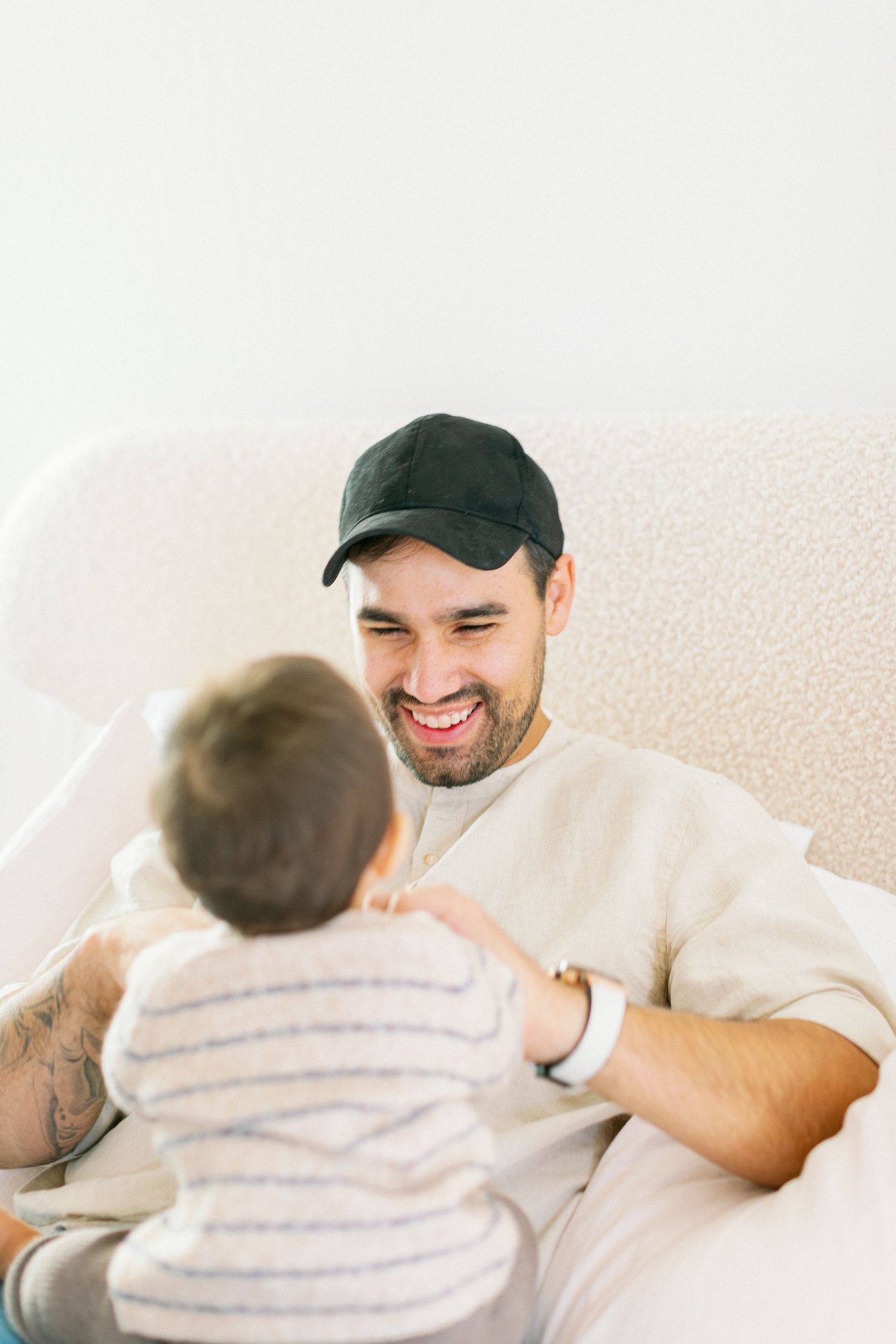 A tender moment shows an adult and young child sharing a joyful interaction while sitting on a light colored couch.