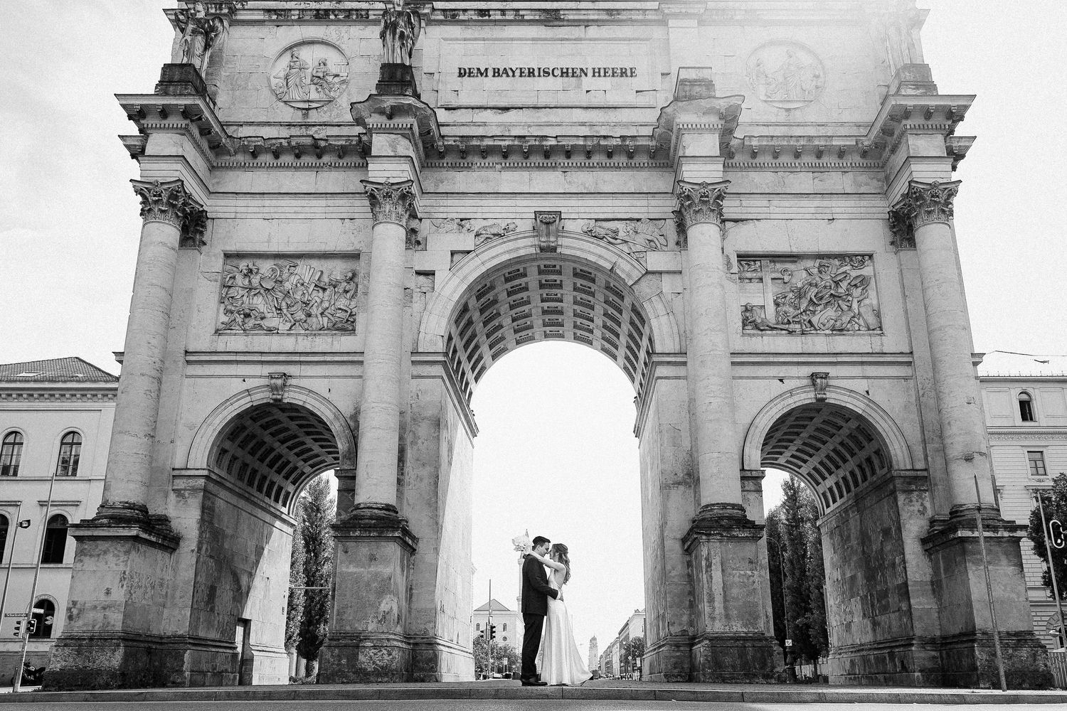 A silhouetted couple stands beneath a grand archway in a black and white architectural photograph.