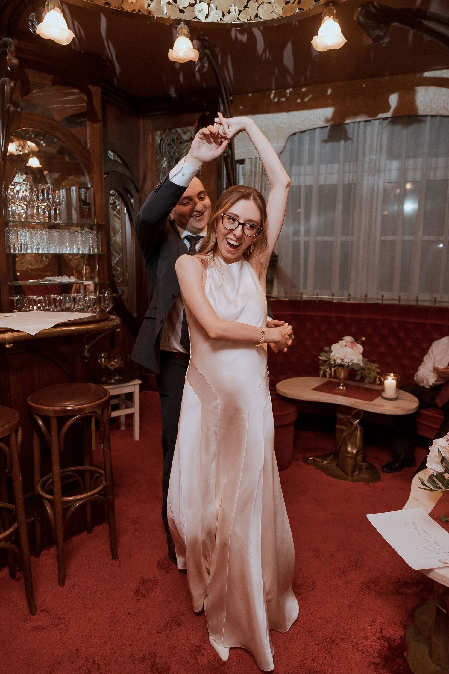 Bride and groom dancing joyfully in elegant red restaurant during wedding reception.