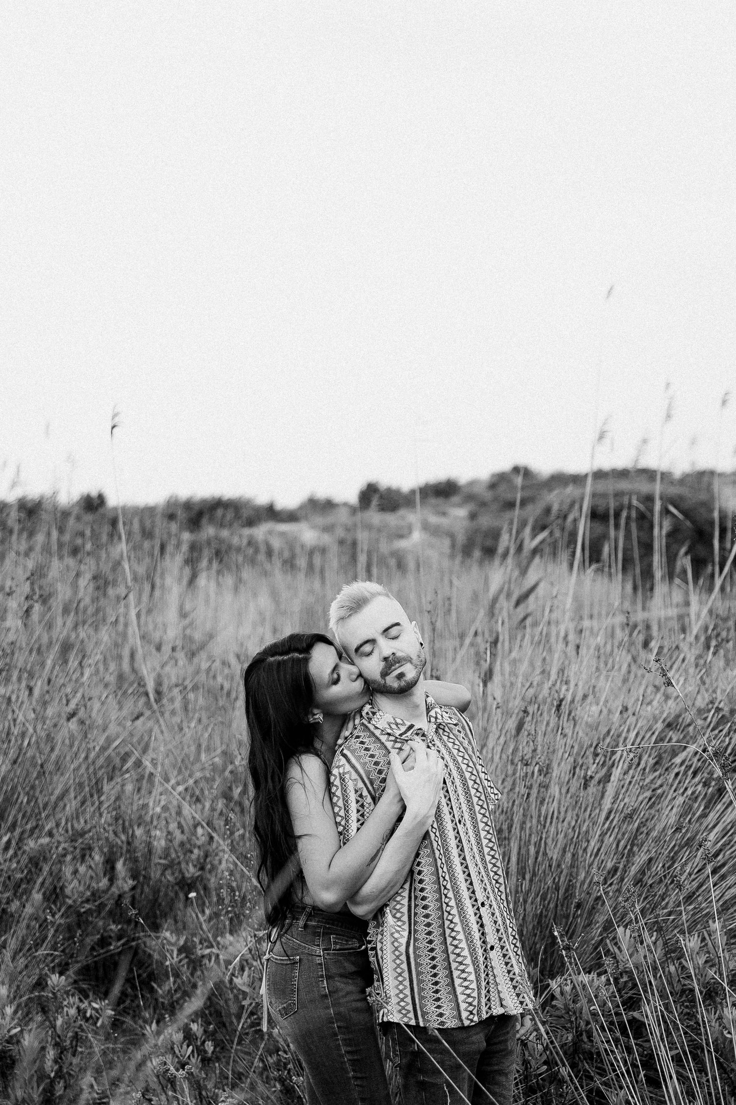 A couple embraces in a field of tall grass during a black and white outdoor photoshoot.