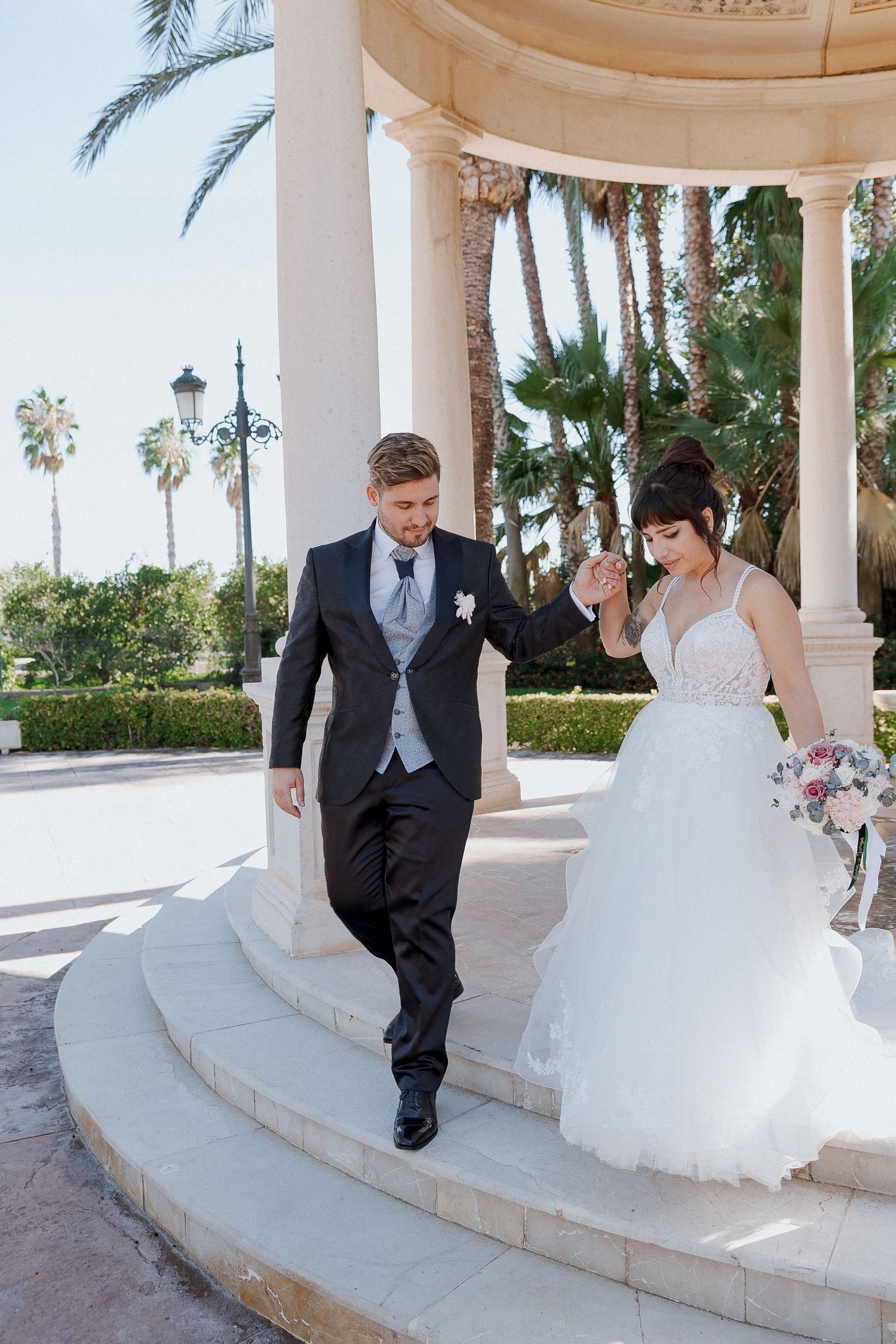 Bride and groom share romantic moments in a white columned gazebo during their wedding photoshoot.