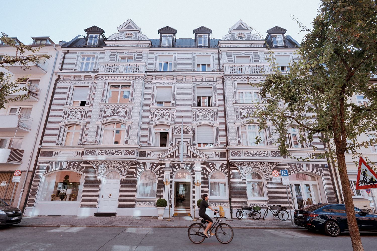 Ornate historic European building facade with decorative white stucco details, cyclist passing on street below.