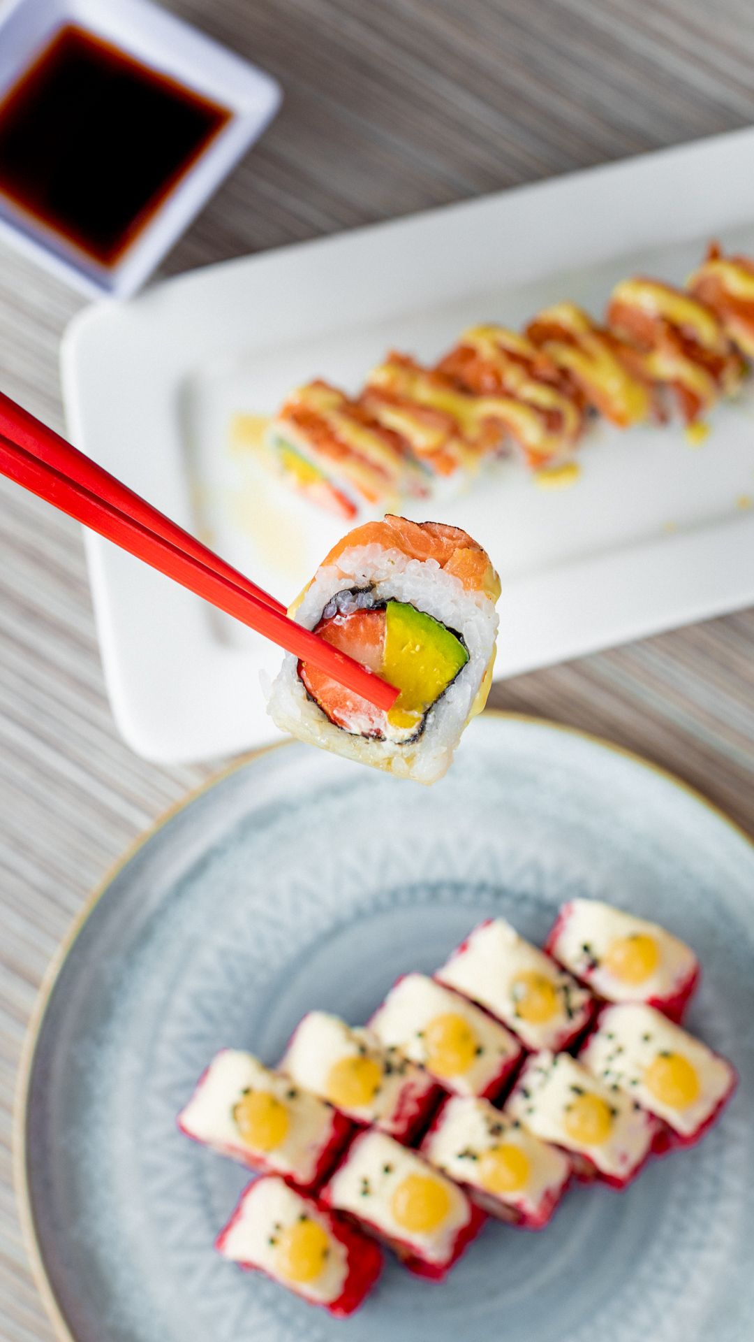 Close-up sequence of colorful sushi rolls being arranged on a light blue plate with red chopsticks.