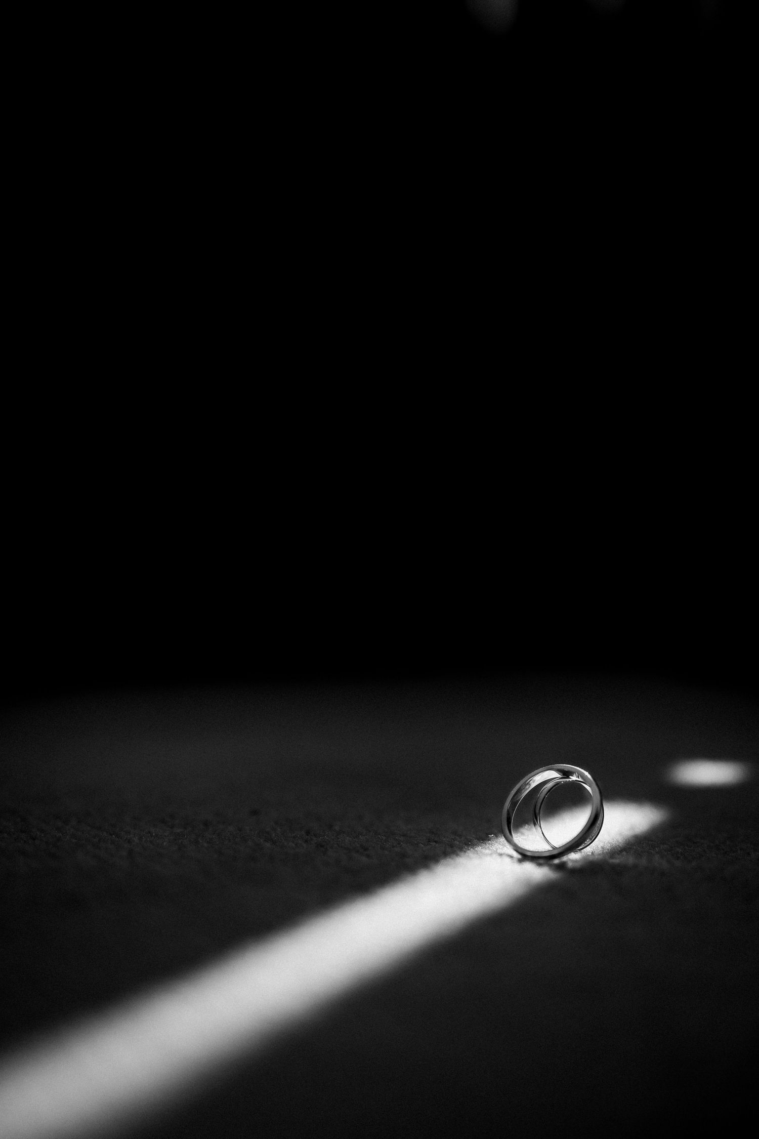 Two wedding rings illuminated by a dramatic beam of light on a dark textured surface.