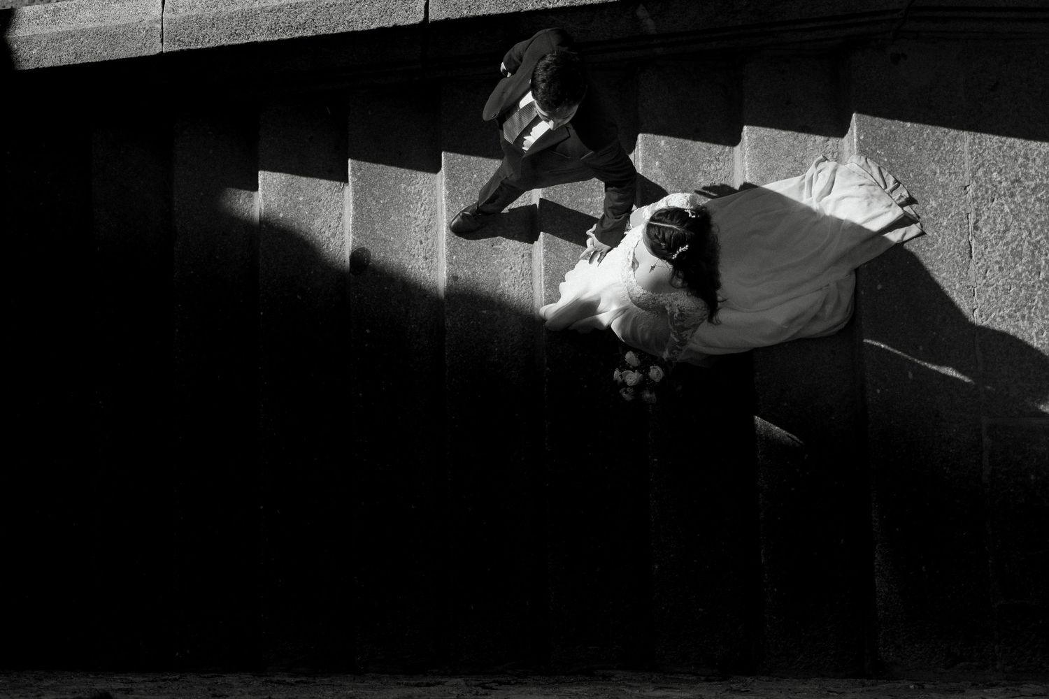 Black and white aerial photo of a person lying on sunlit stone steps in dramatic shadow and light contrast.