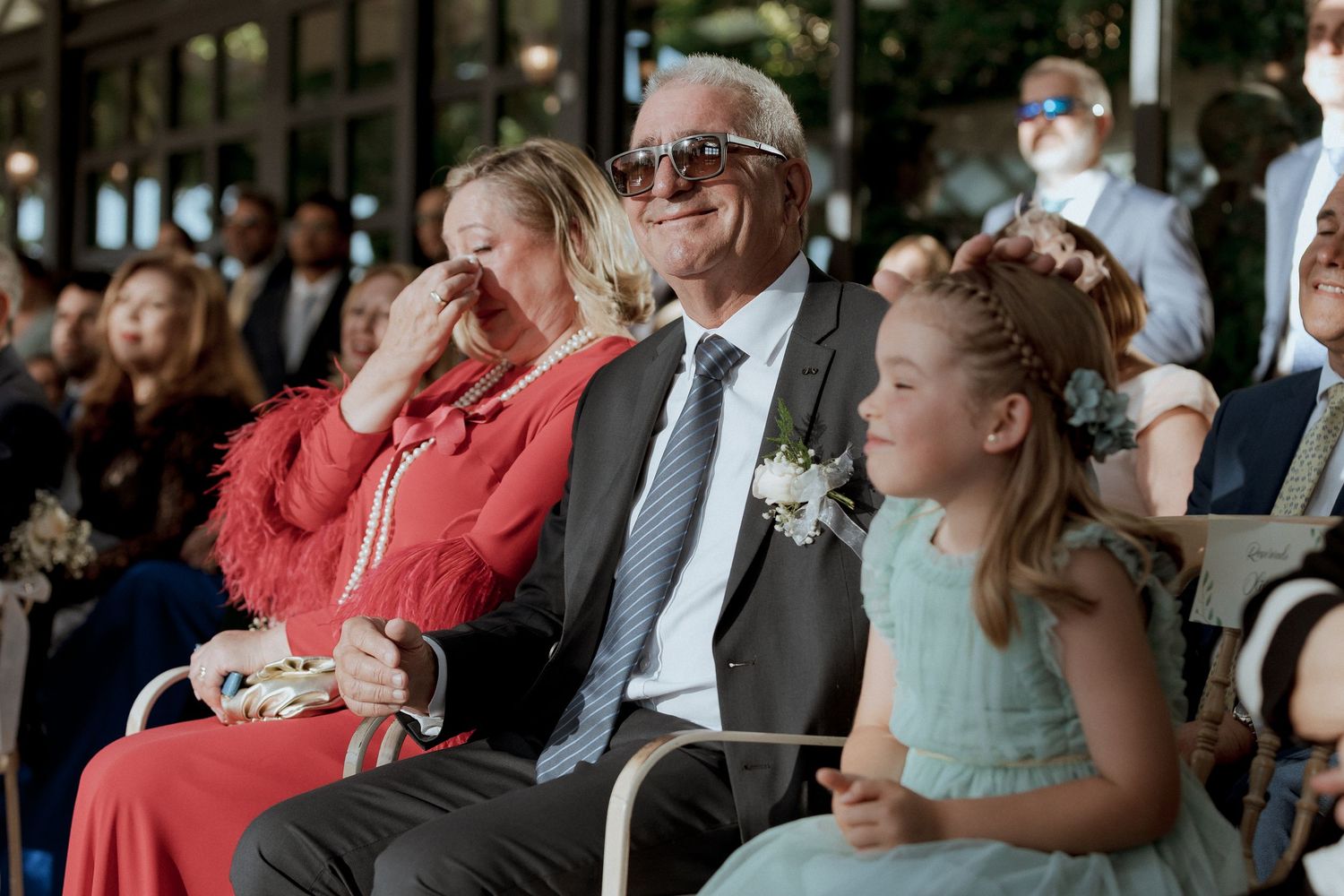 Emotional wedding guests including an older man and young flower girl watching the ceremony.