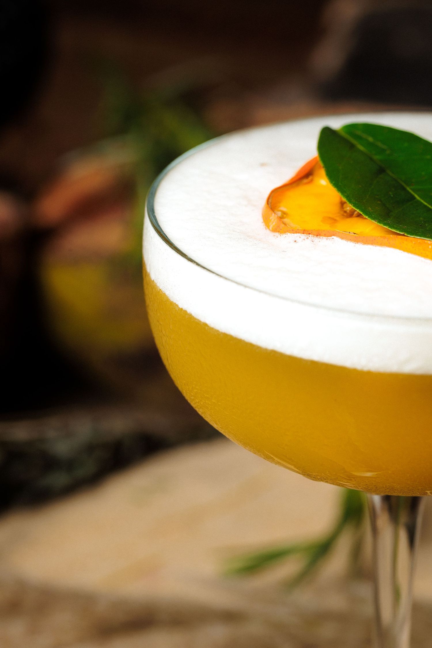 A close-up shot of a yellow cocktail garnished with an orange peel and green leaf in a martini glass.