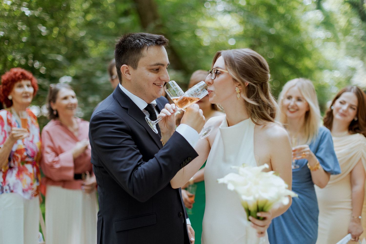 Newlyweds sharing a champagne toast with smiling guests celebrating outdoors after their wedding ceremony.