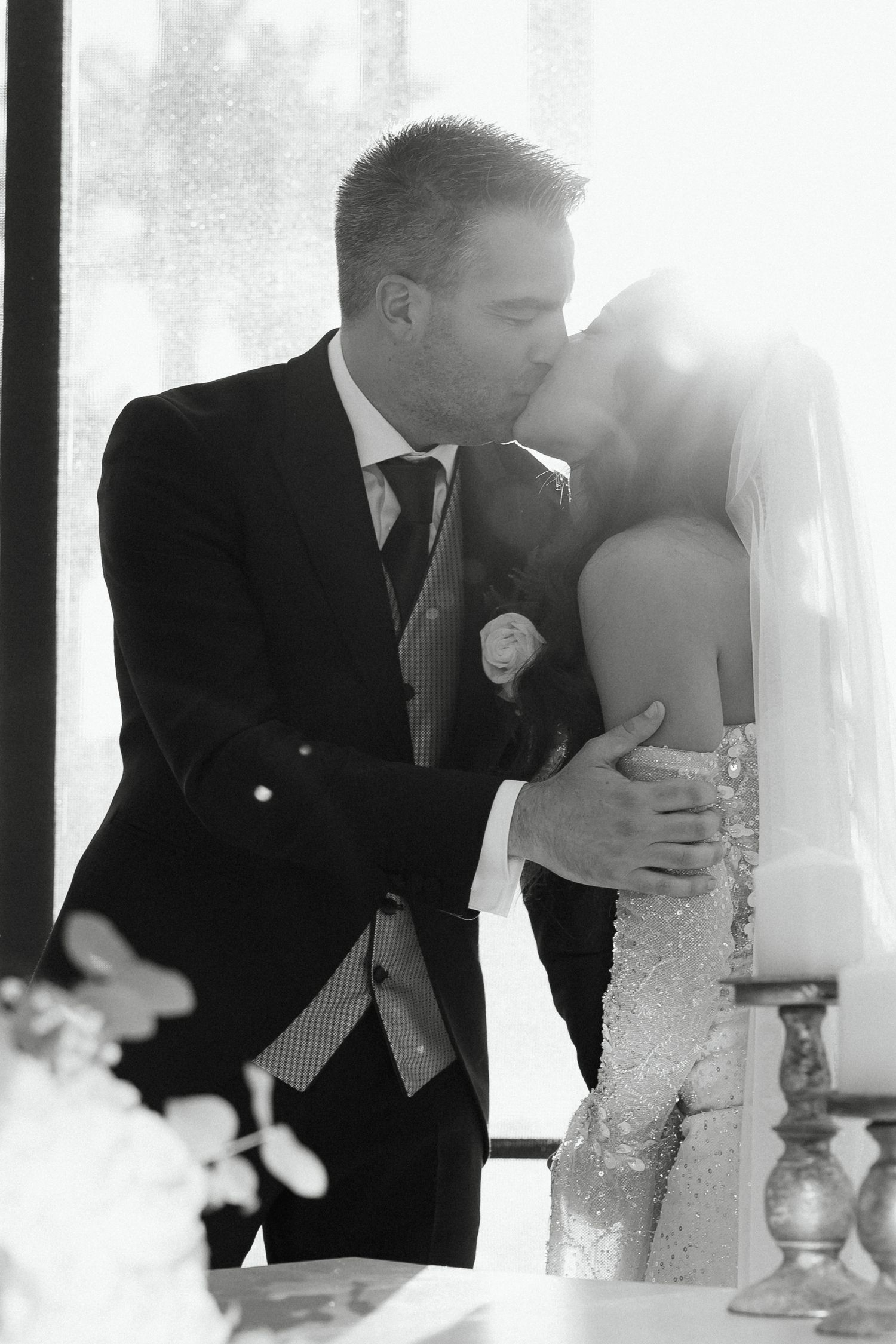 Black and white photo of bride and groom sharing their first kiss at the altar.