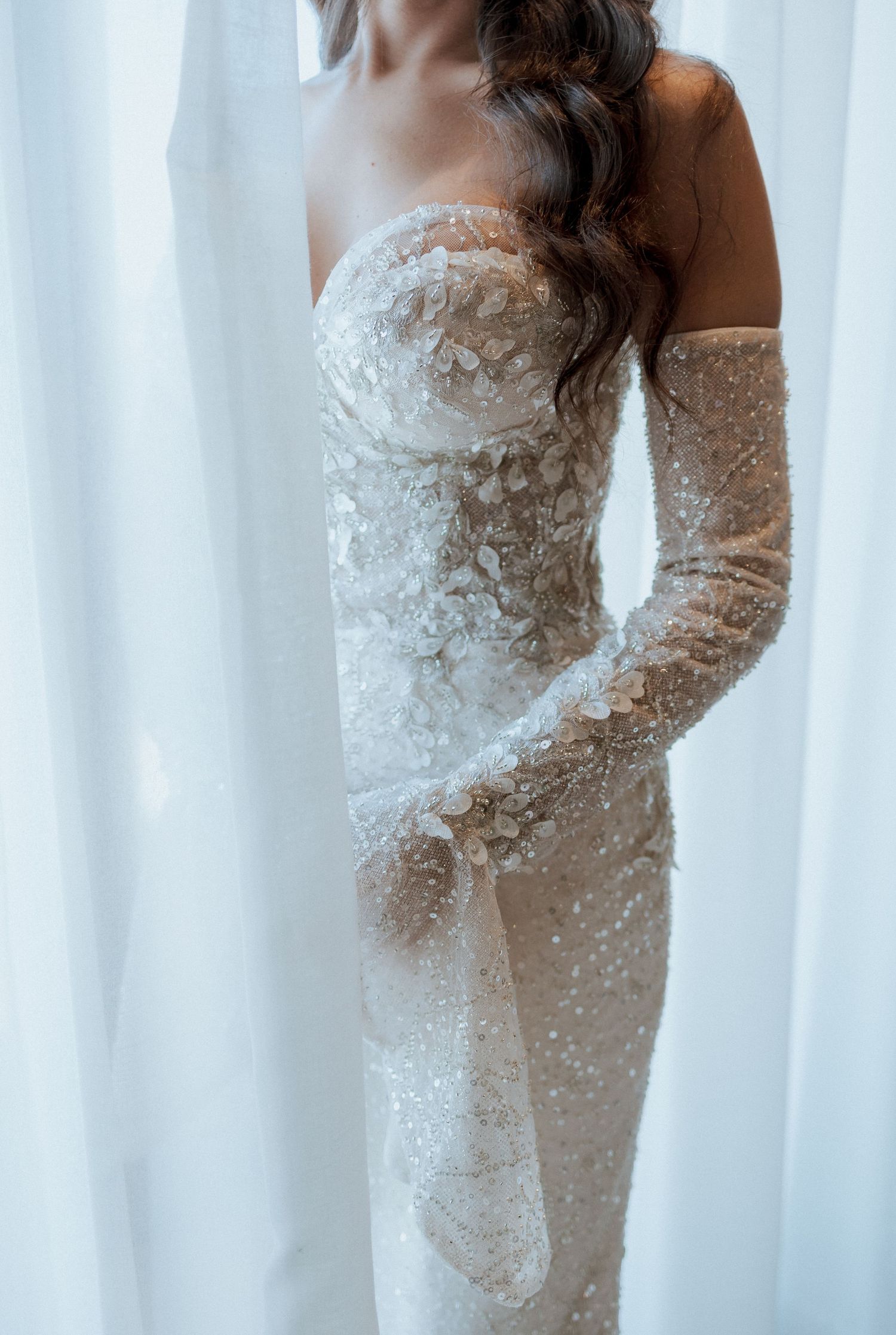 Bride in a stunning beaded strapless wedding gown with sheer gloves and floral embroidery.