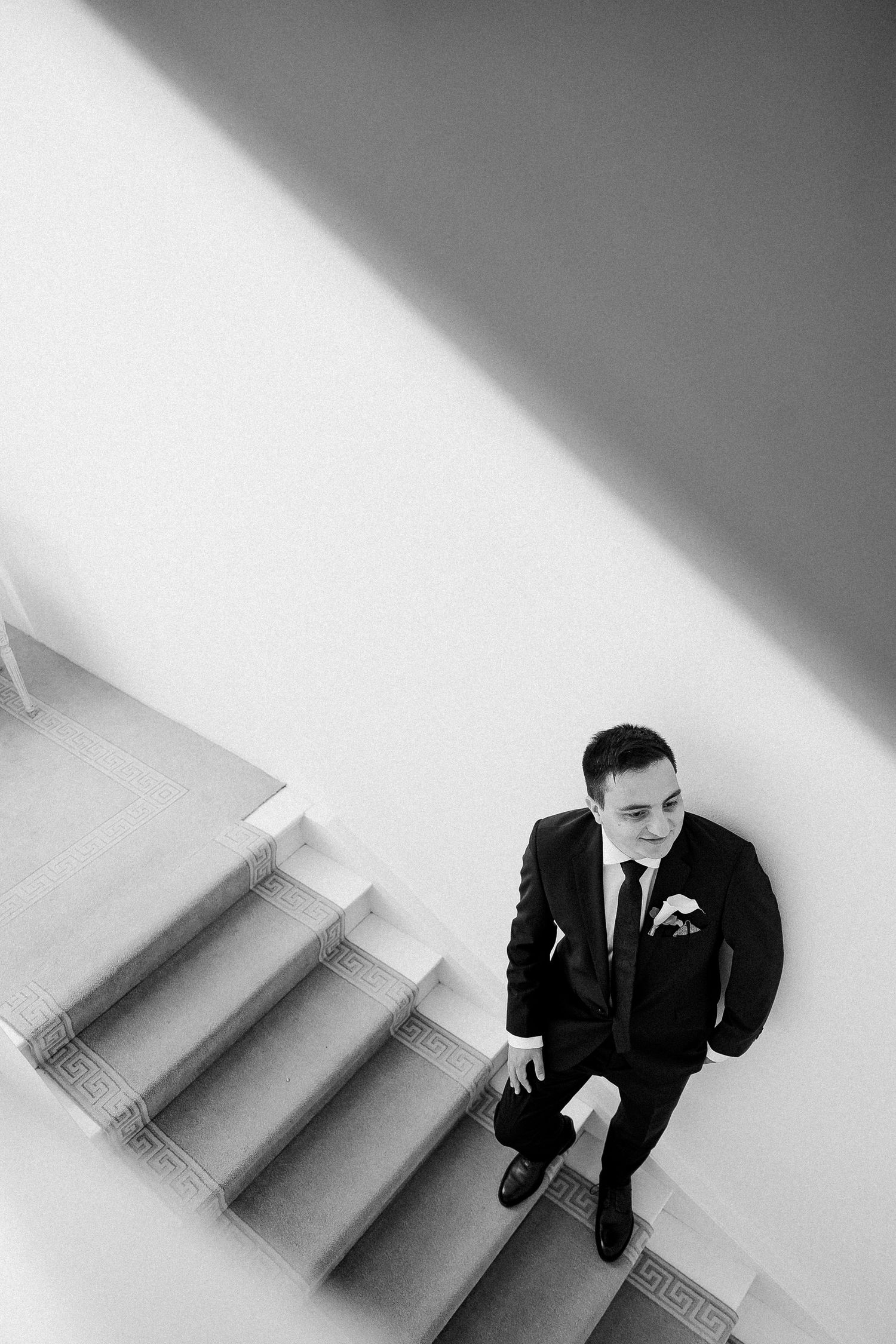 Black and white aerial view of groom in suit standing on staircase with boutonniere.