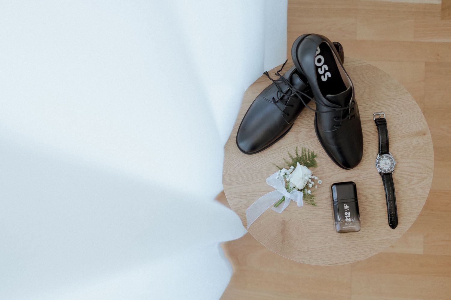 Black Hugo Boss dress shoes with boutonniere, watch, and cologne on wooden tray for wedding day groom accessories.