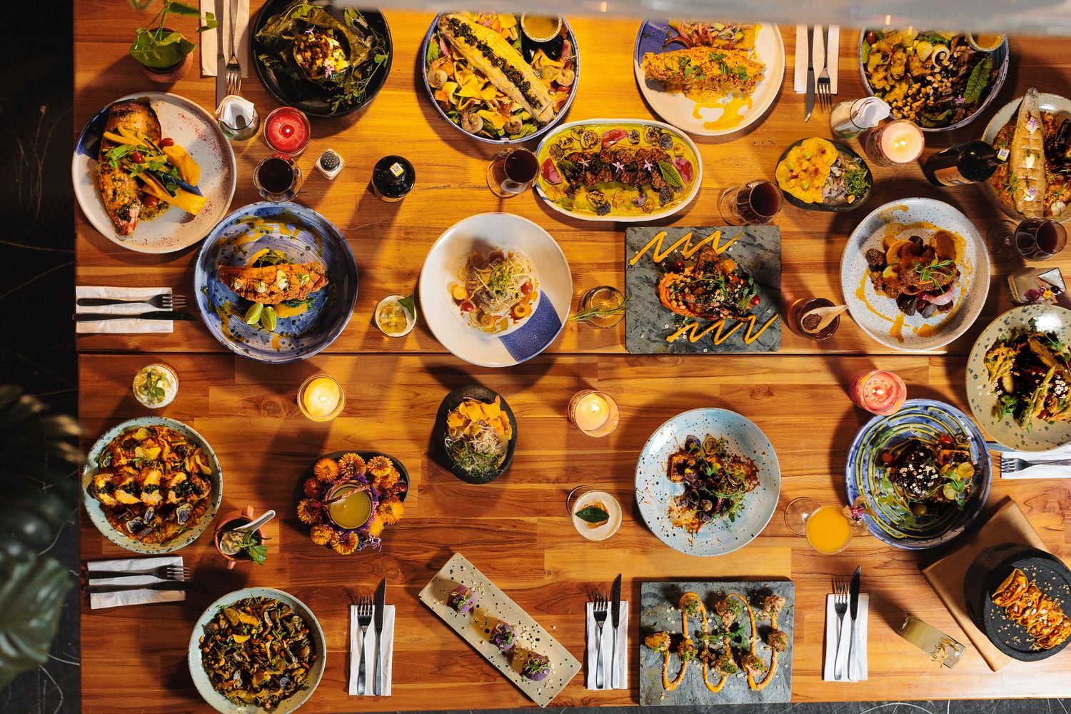 Overhead view of multiple plates of Asian cuisine on a wooden table with chopsticks and dim lighting.
