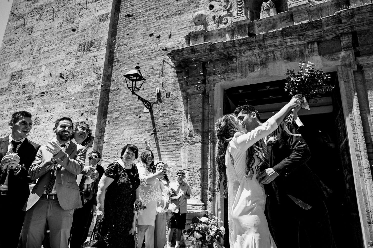 Wedding party celebrates joyfully on outdoor stone patio during daytime reception.