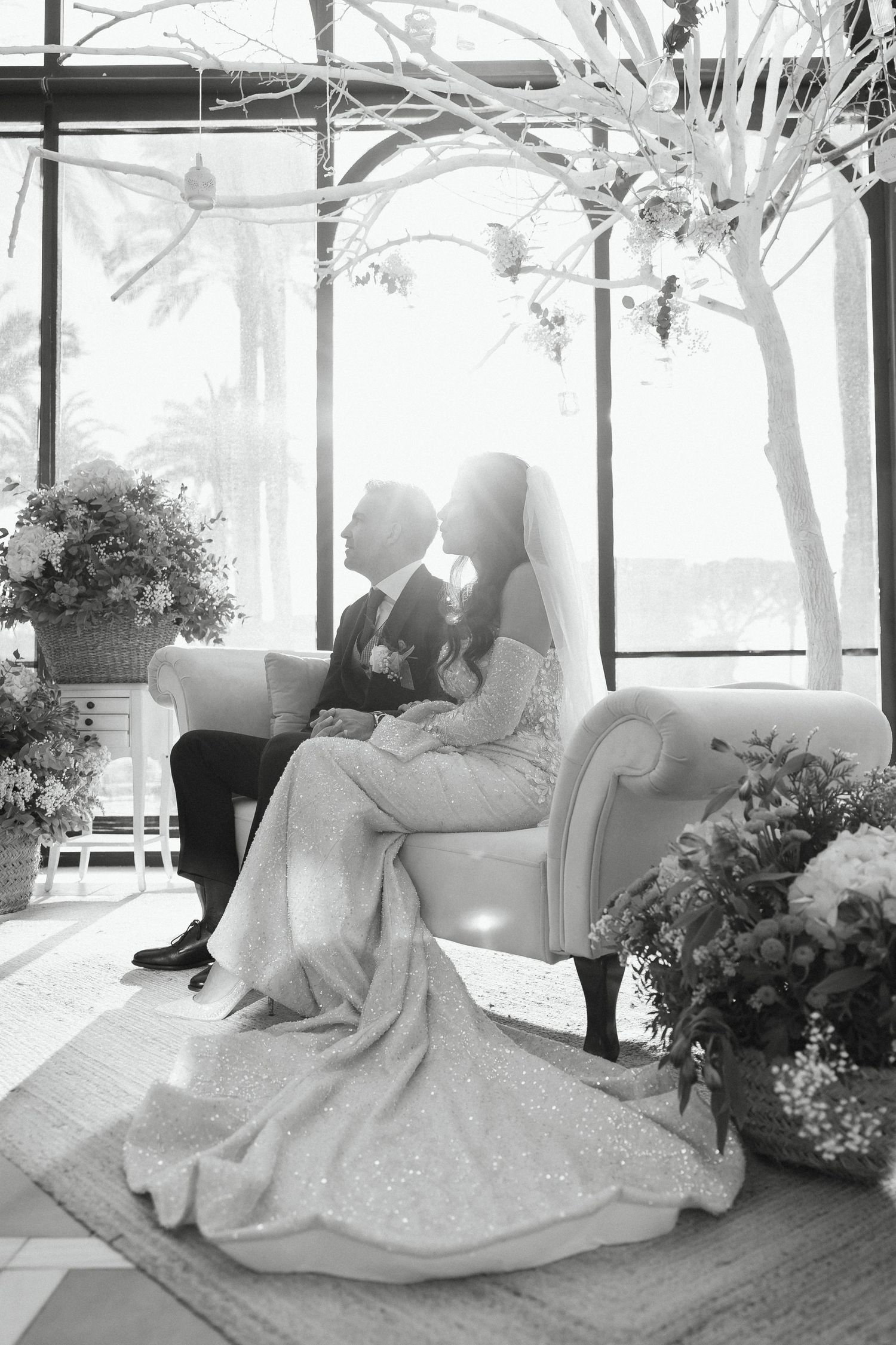 Black and white photo of bride and groom sharing a romantic moment seated on a sofa.