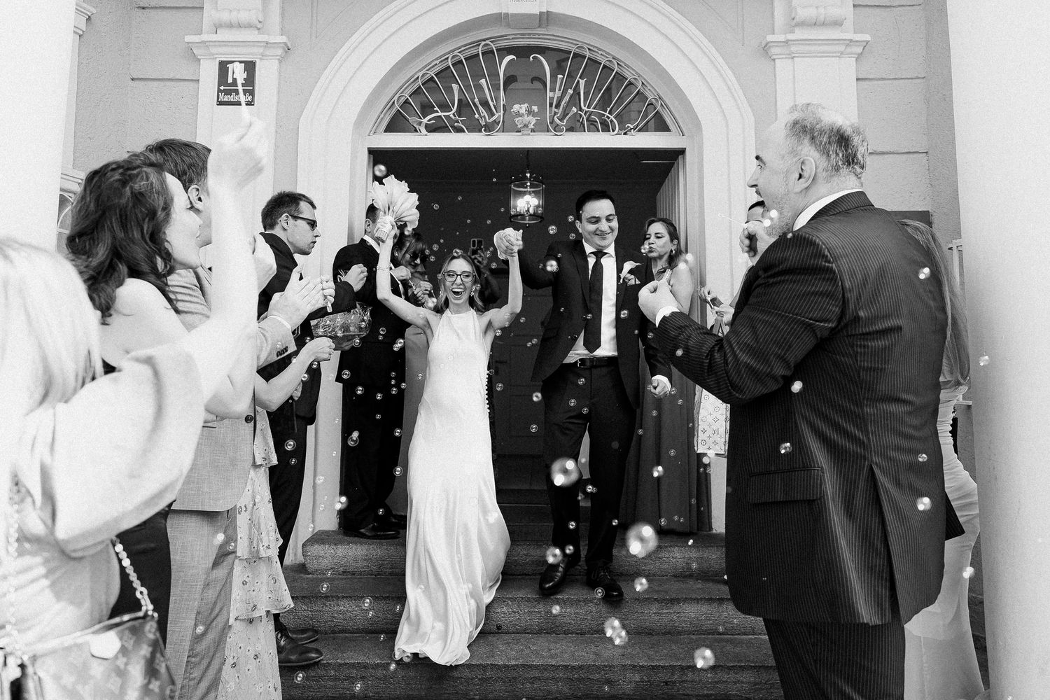 Bride and groom exit church doors as guests throw confetti in joyful black and white wedding celebration photo.