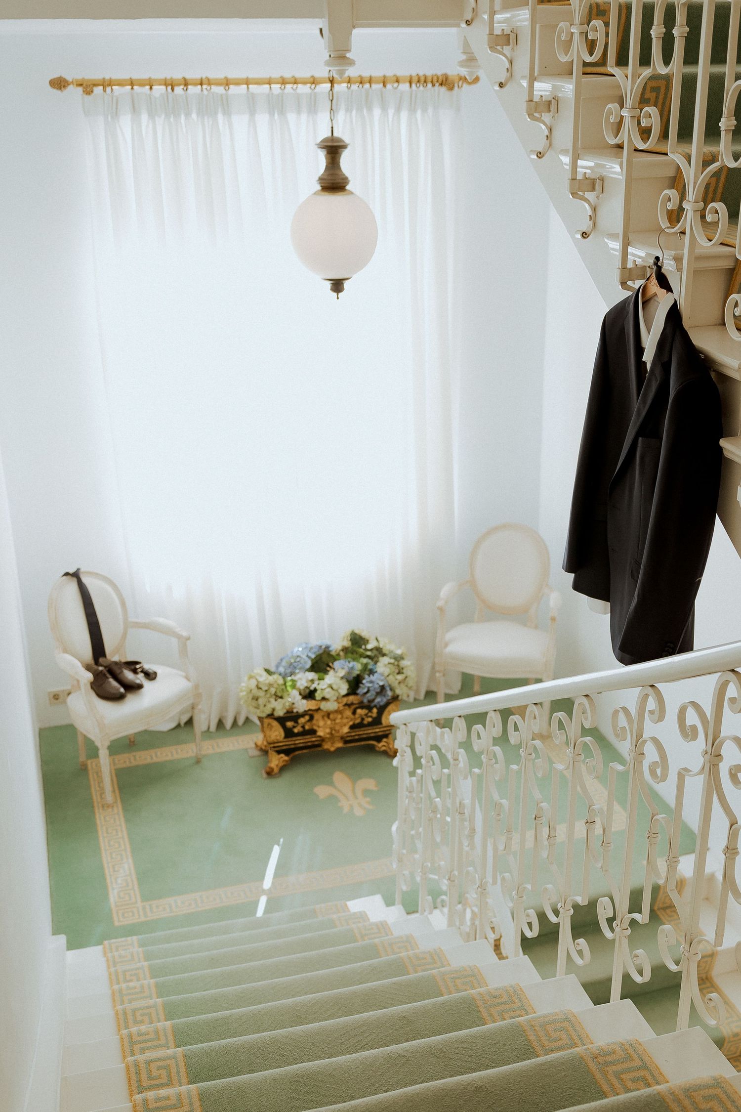 Elegant wedding venue staircase with ornate white railings, mint green carpet, and groom's suit hanging nearby.