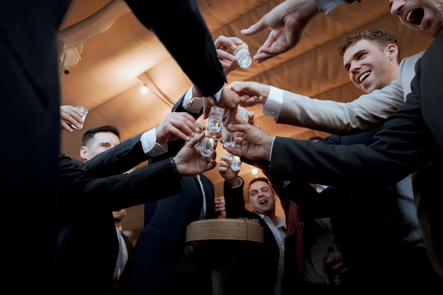 Groomsmen toasting with glasses of whiskey at a wedding celebration.