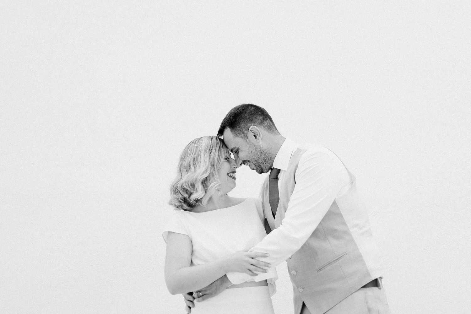 A romantic black and white portrait of a couple embracing in an intimate moment against a plain white backdrop.