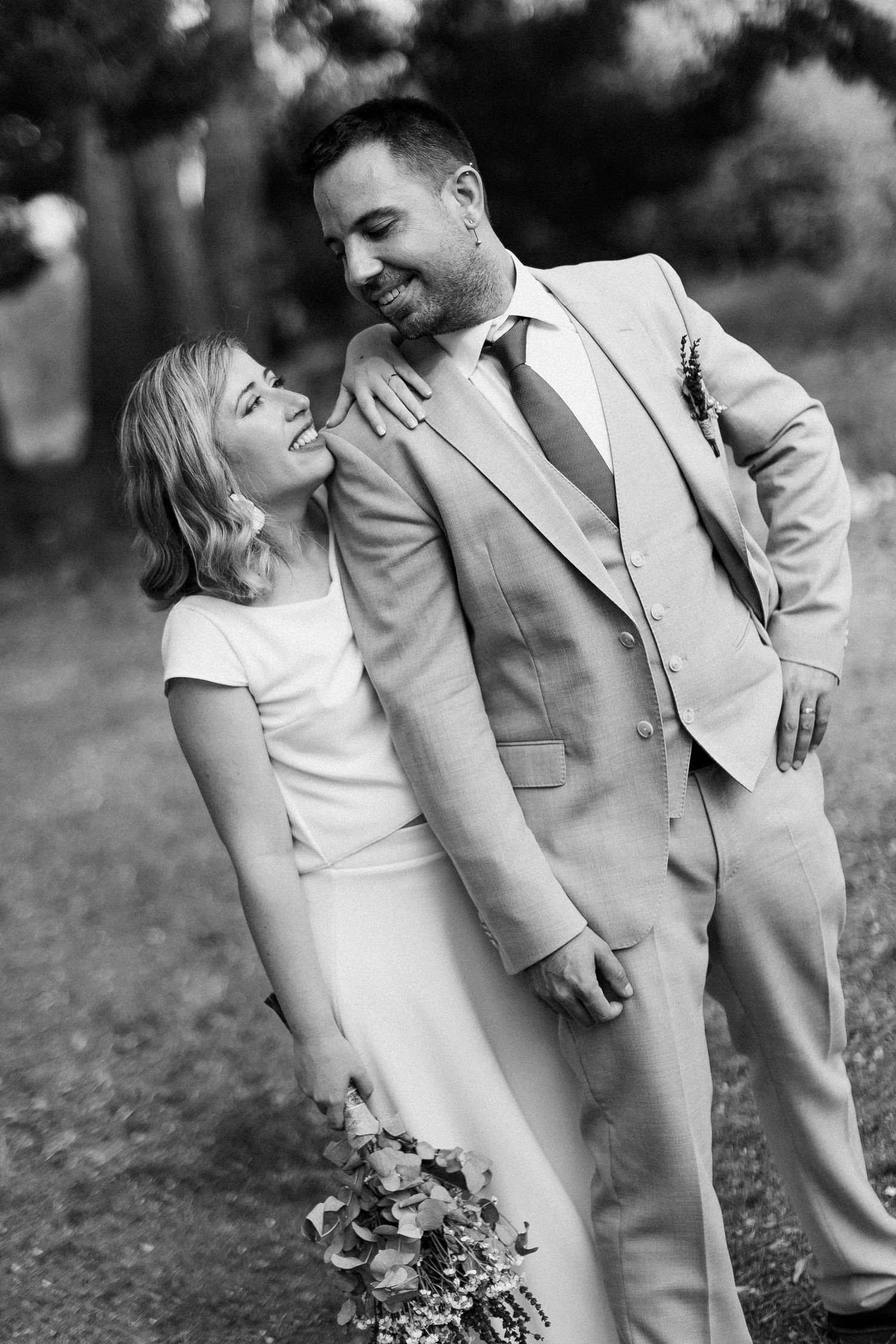 A joyful bride and groom share a candid laughing moment in black and white, with the bride holding a floral bouquet.